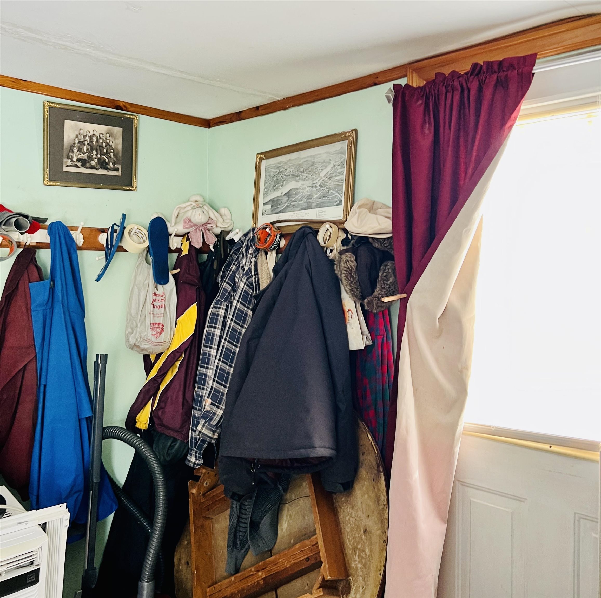 Entryway with coats and hats on wall hooks beside a bright curtained window.
