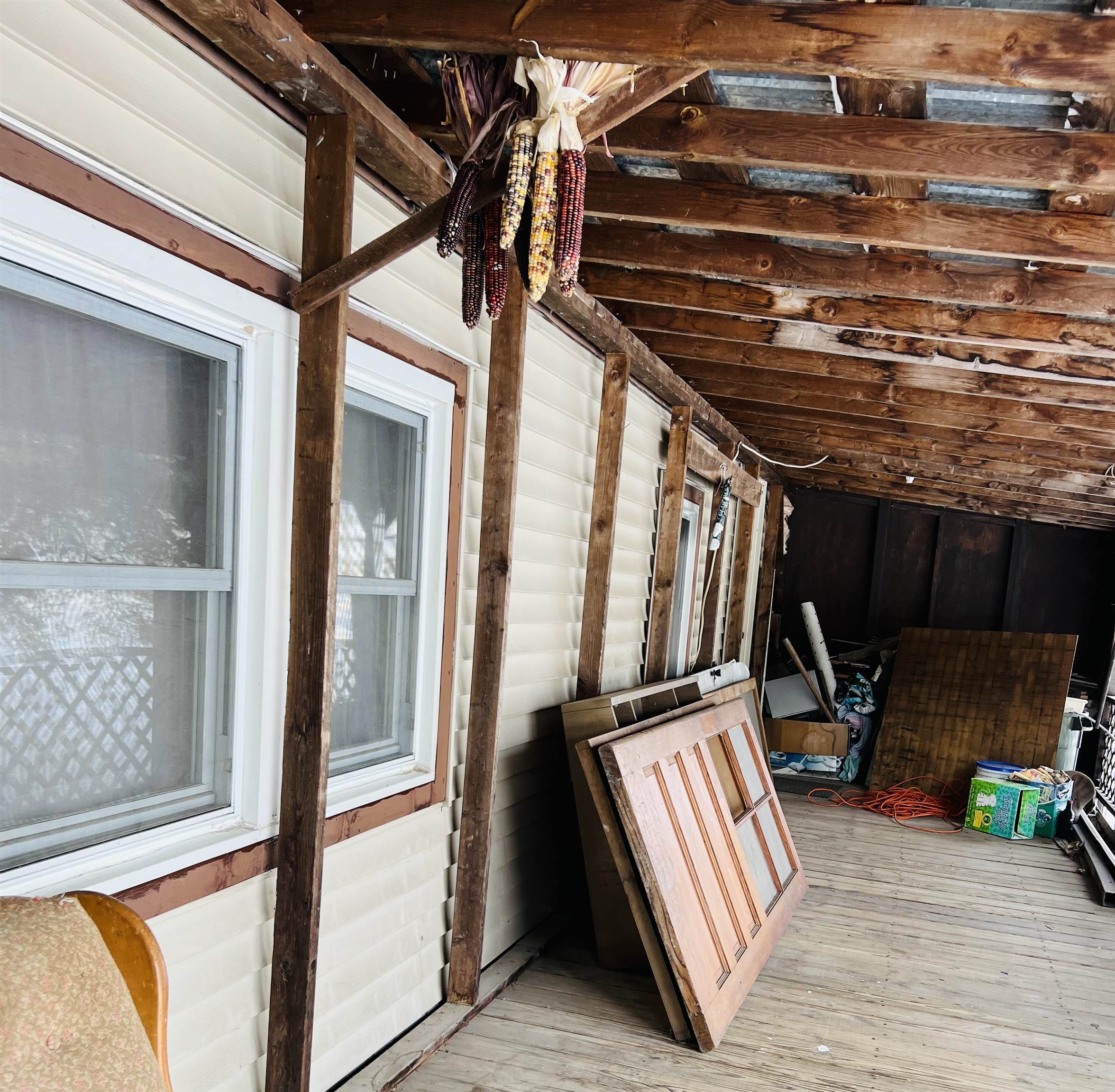 Covered porch with exposed wooden beams, stored doors, and colorful dried corn hanging overhead.