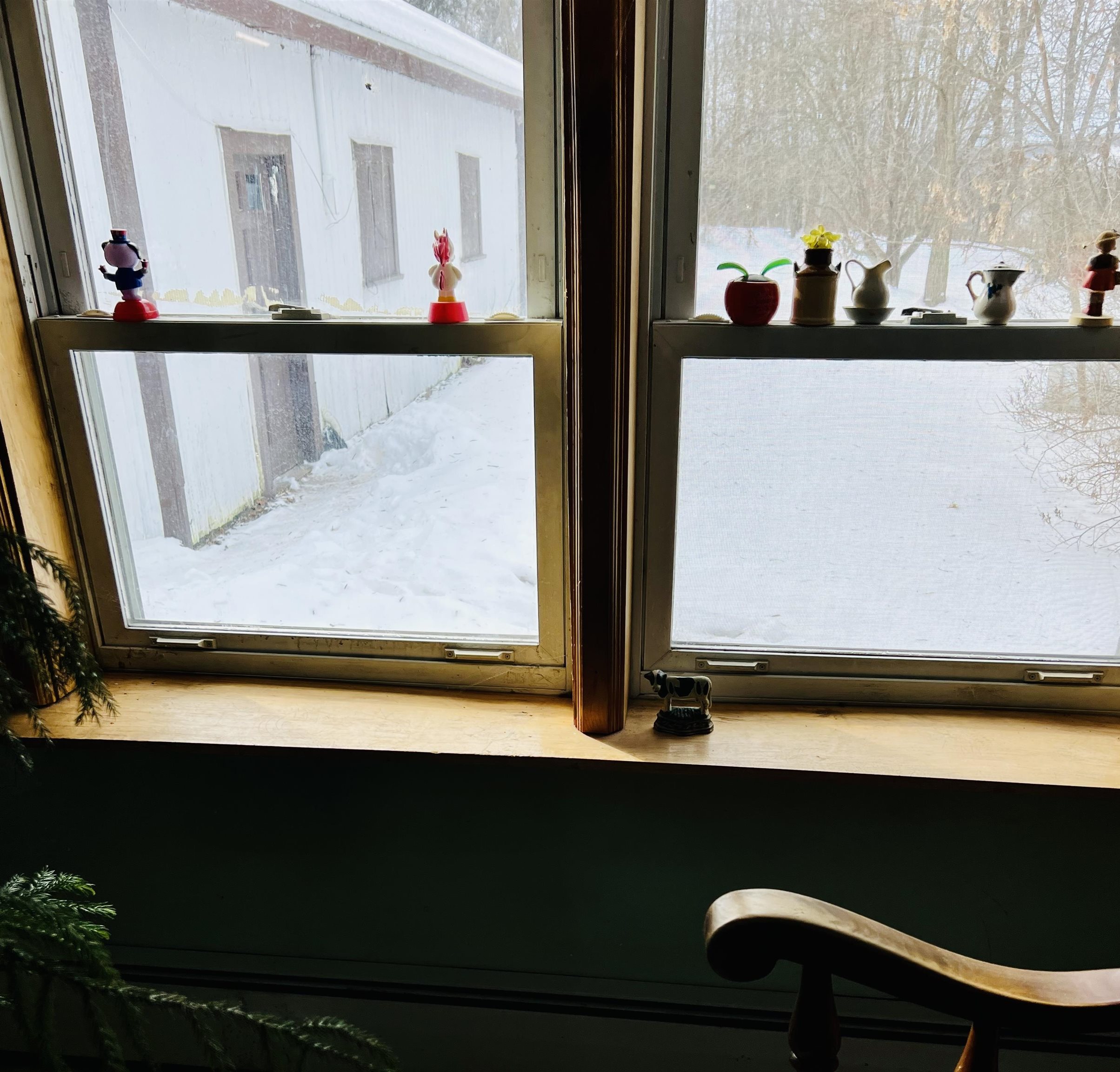 Interior window with figurines on the sill overlooking a snowy yard and neighboring white building.