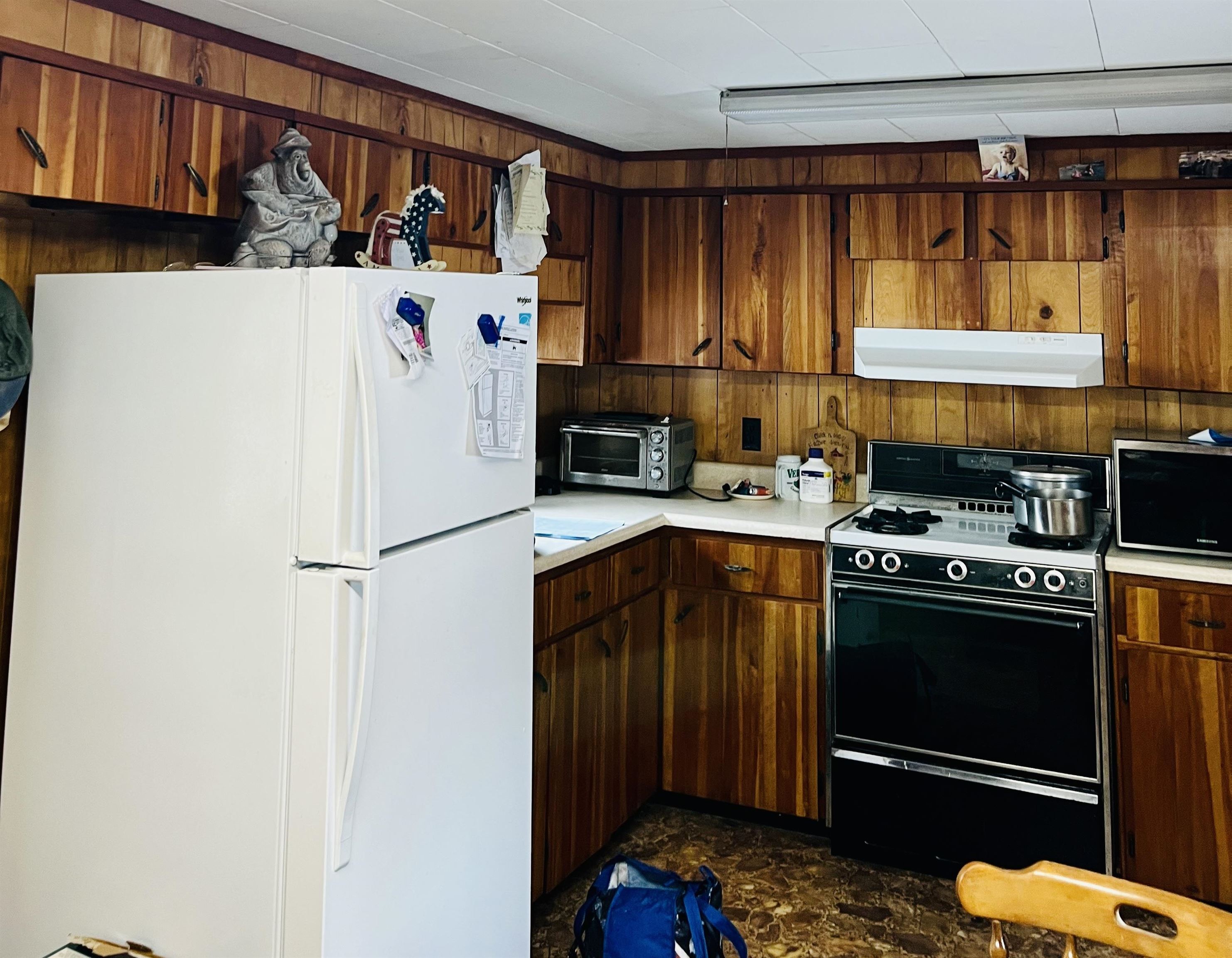 Kitchen with wood-paneled cabinets, a white refrigerator, and black gas range.