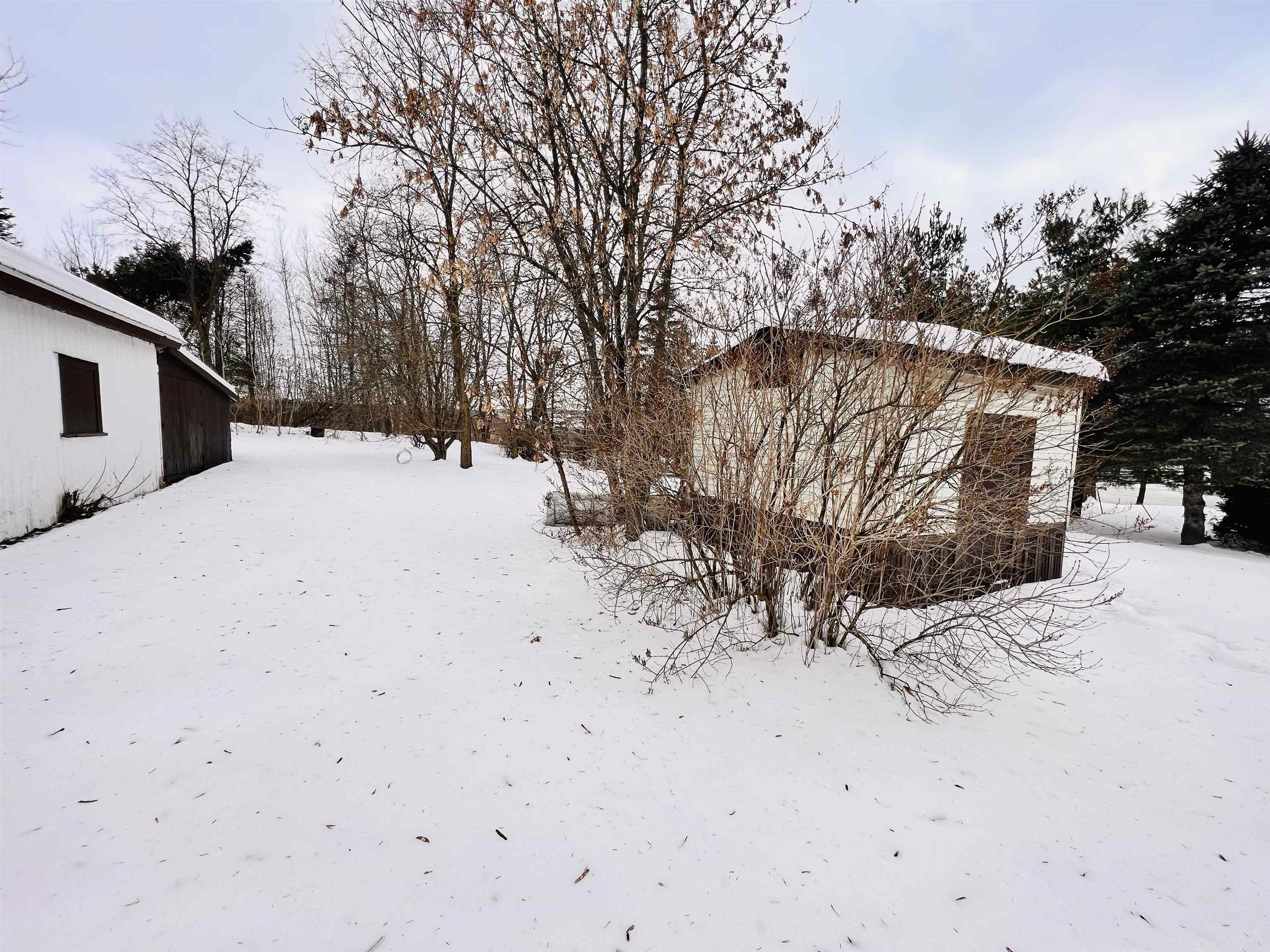Snow-covered yard with small outbuildings and leafless shrubs.