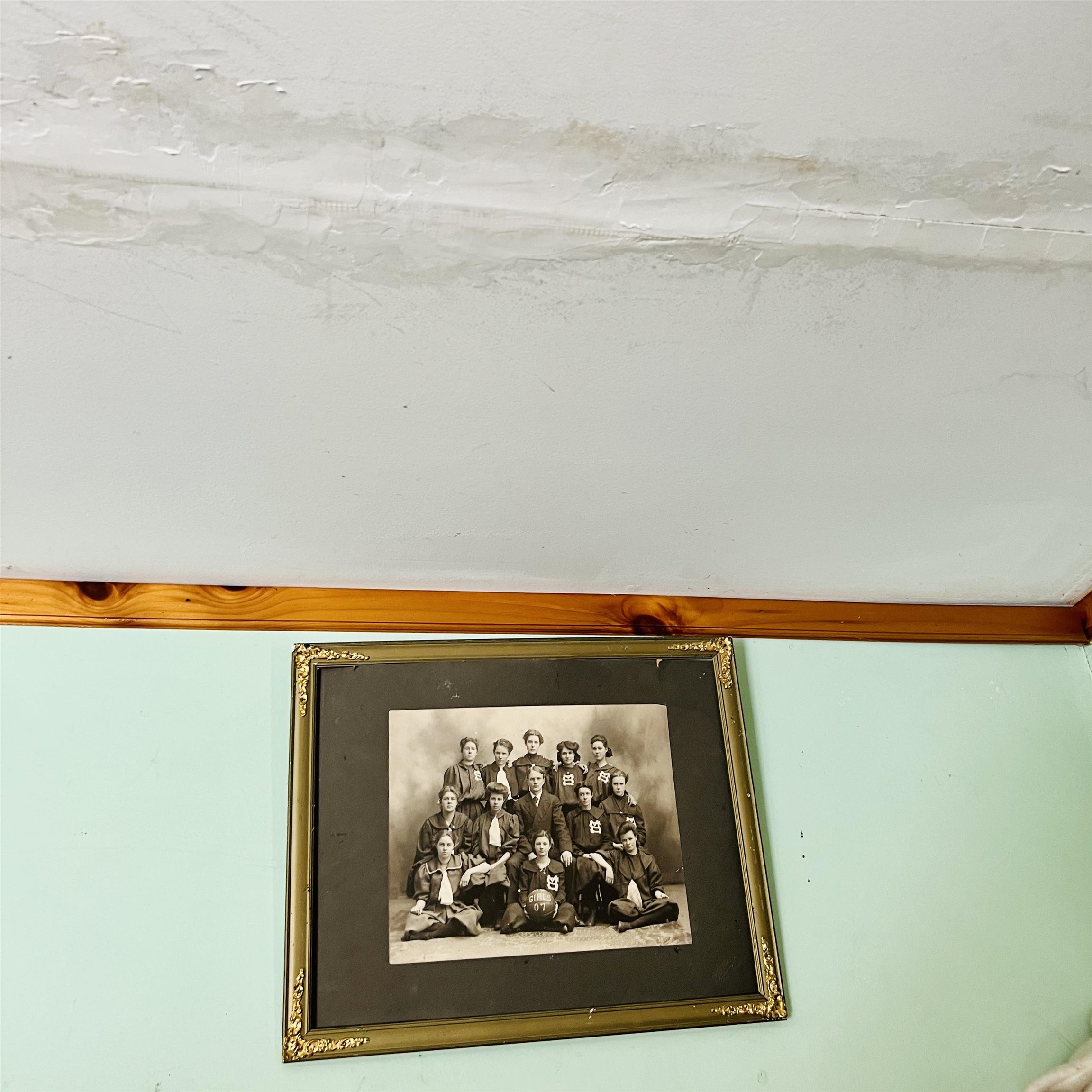 Mint-green interior wall with an ornate framed vintage group portrait beneath wood trim.
