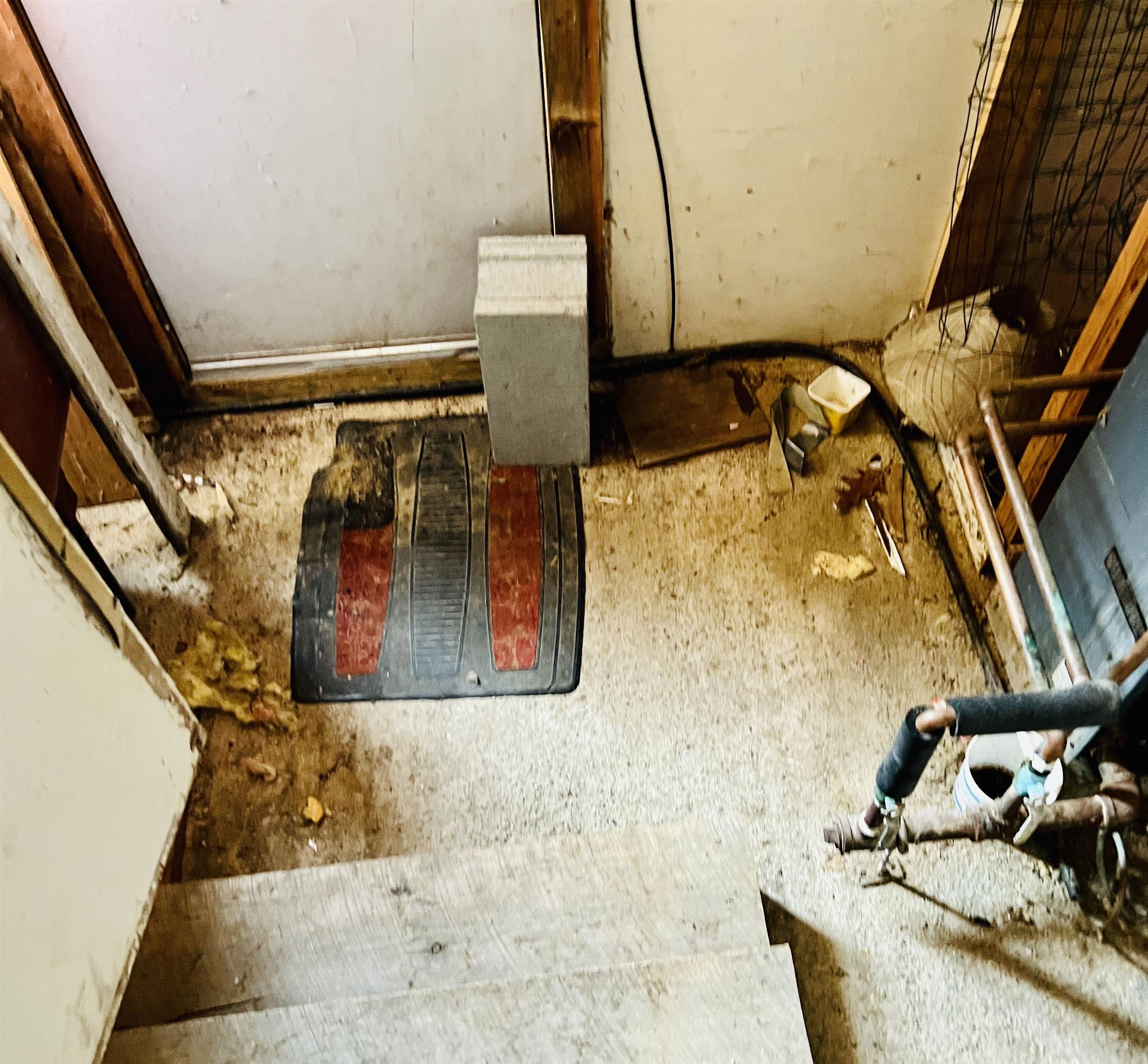 Unfinished basement with exposed framing, pipes, a concrete floor, and wooden stairs.