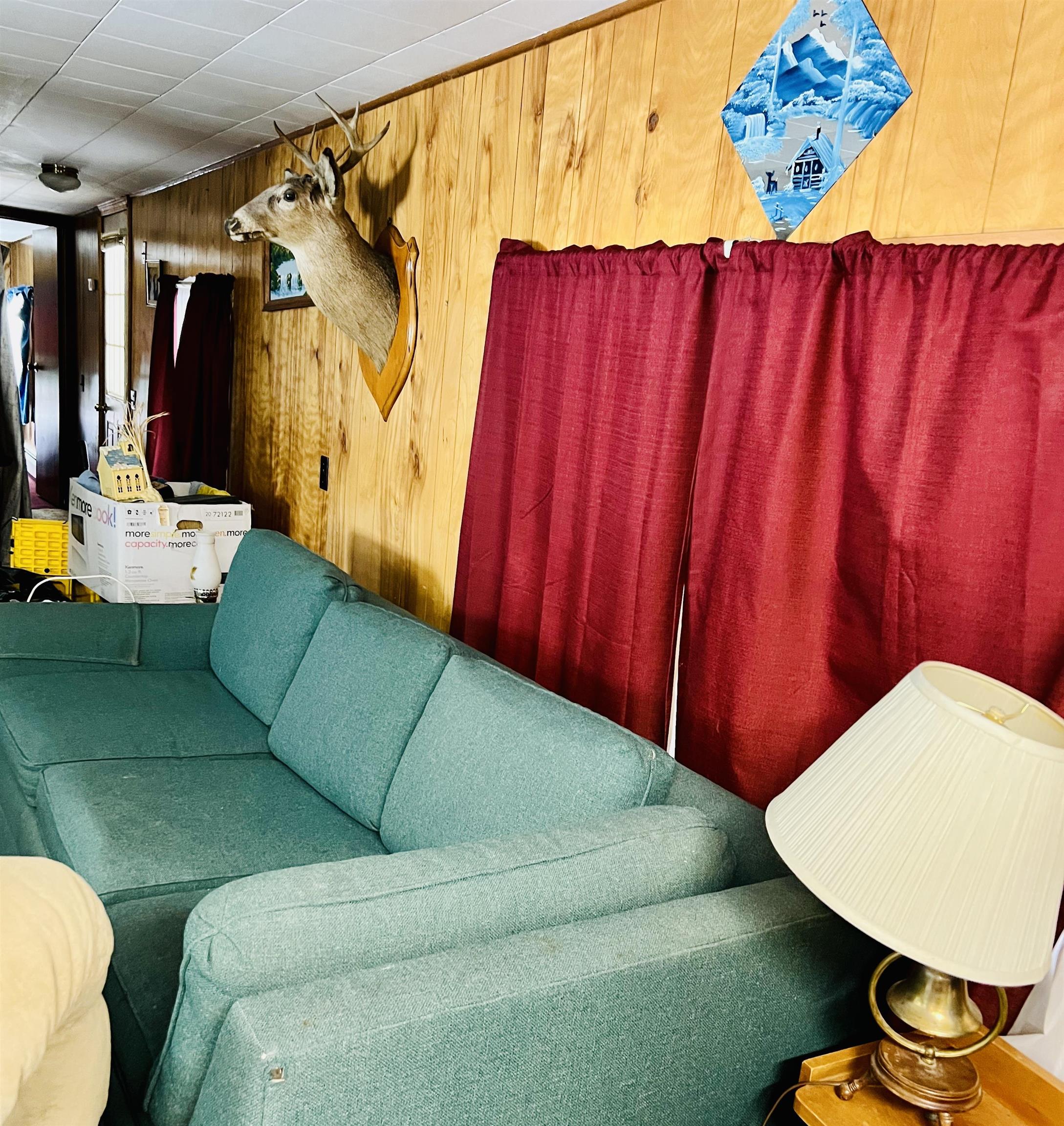Living room with a teal sectional, wood-paneled walls, red curtains, and a mounted deer head.
