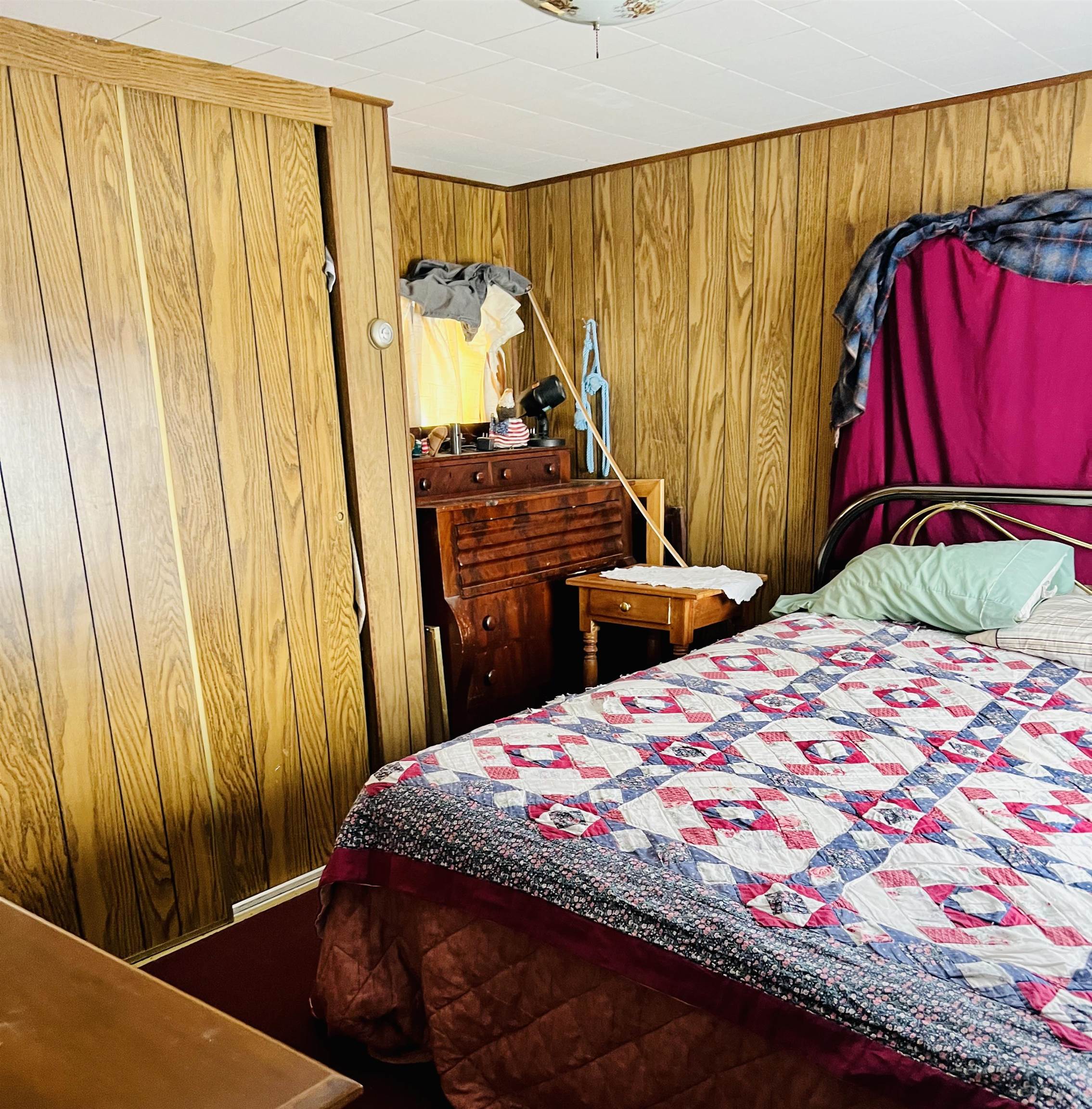Bedroom with wood-paneled walls, wooden dressers, and a red, blue, and white patchwork quilt.