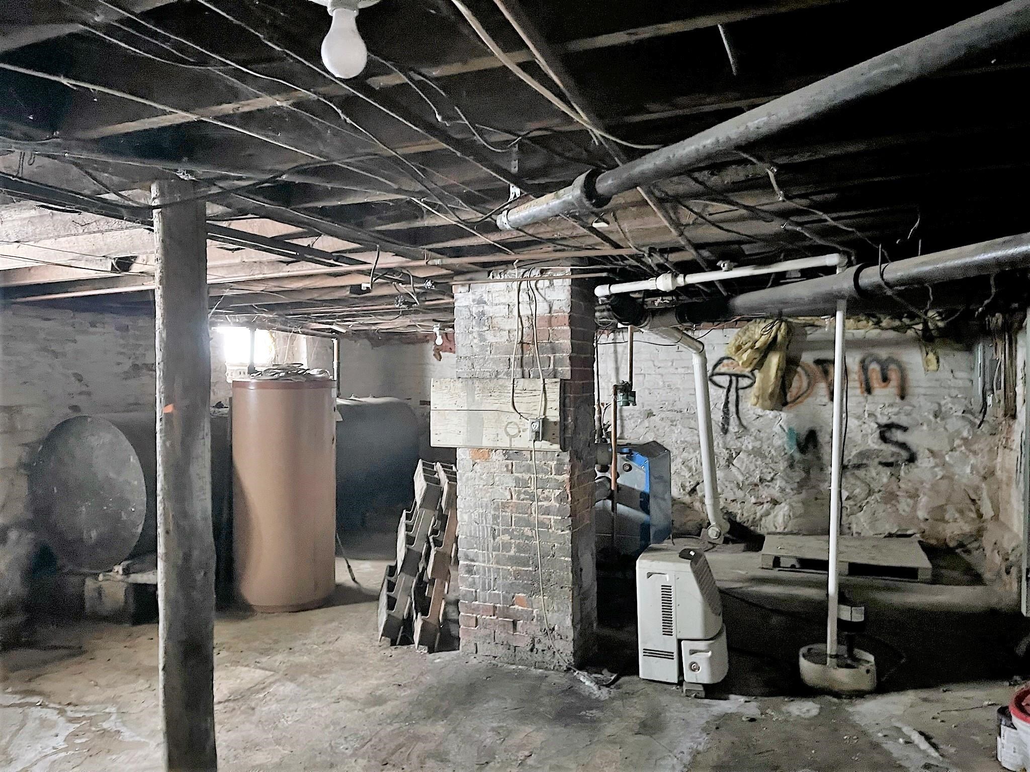 Unfinished basement with exposed pipes, brick support columns, and heating equipment.