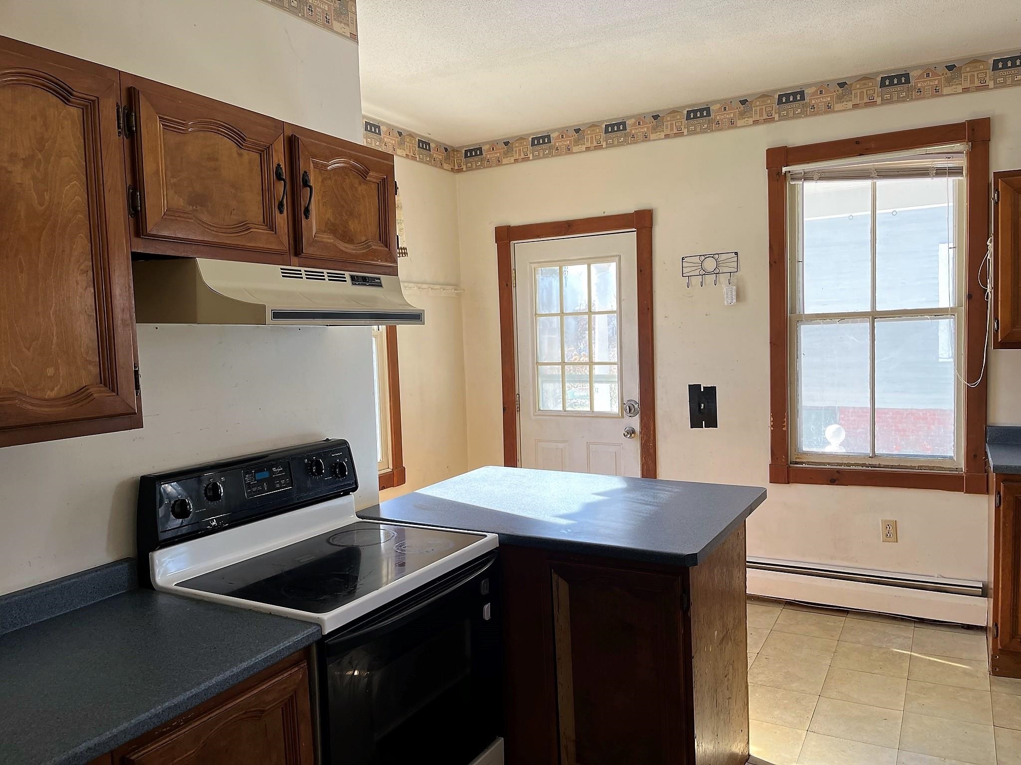 Kitchen with dark wood cabinets, a central island, electric range, and a glass-paneled door beside a large window.