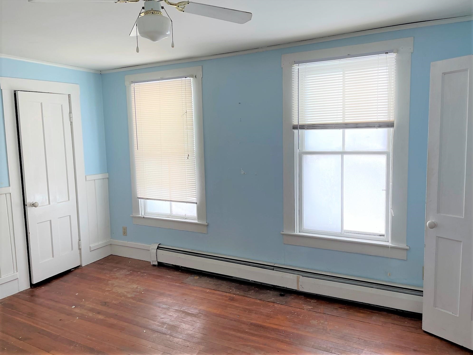 Empty blue room with hardwood floors, two windows, and white paneled doors.