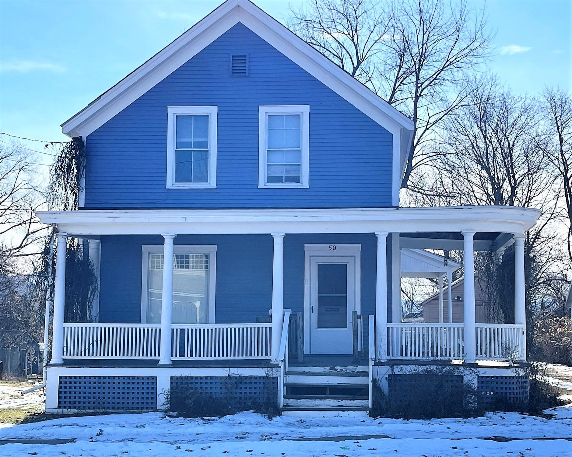 Blue two-story house with white trim and a wide covered porch, photographed with snow on the ground.