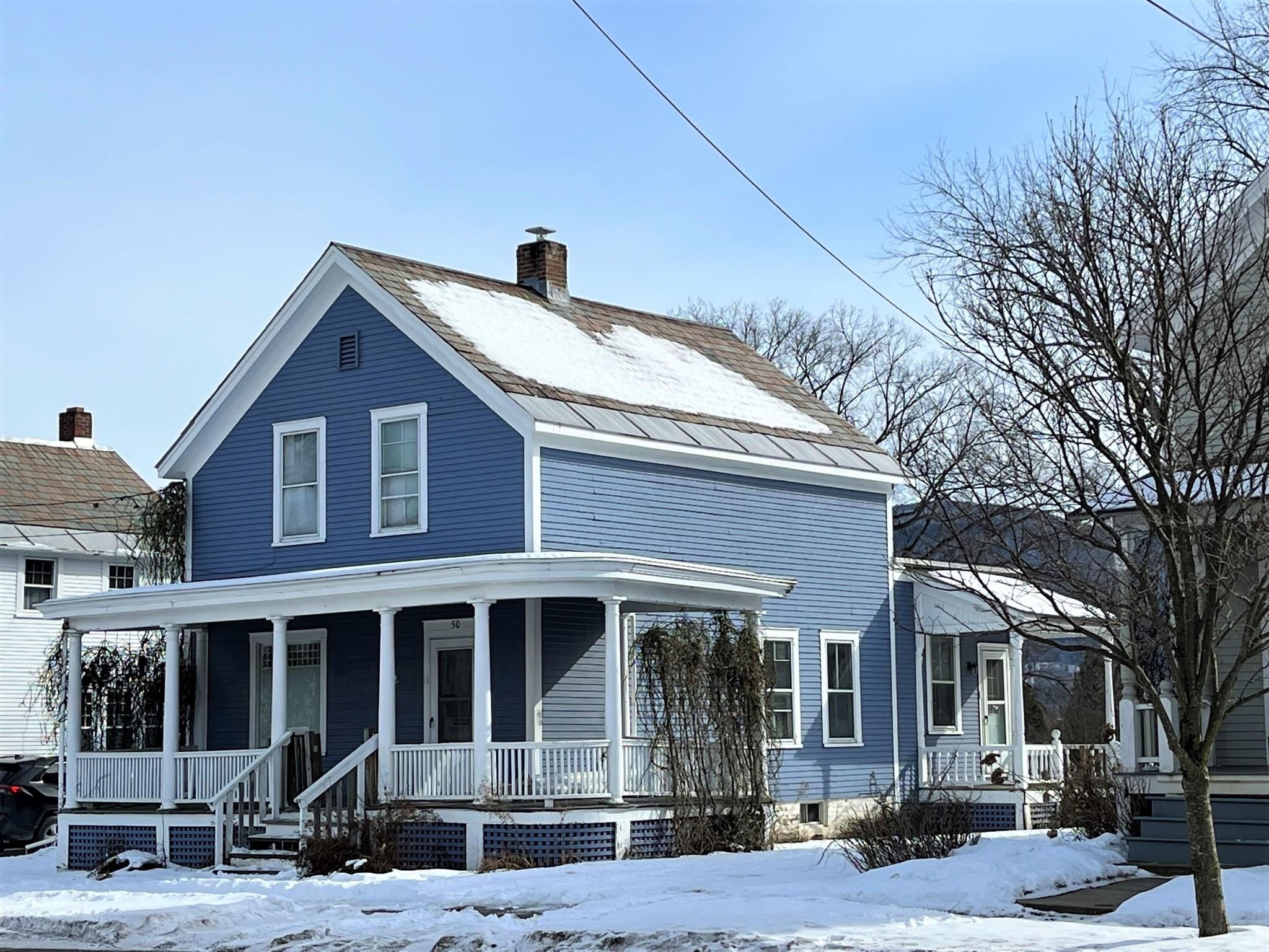 Blue two-story house with a broad white-columned porch and snow-covered roof and yard.