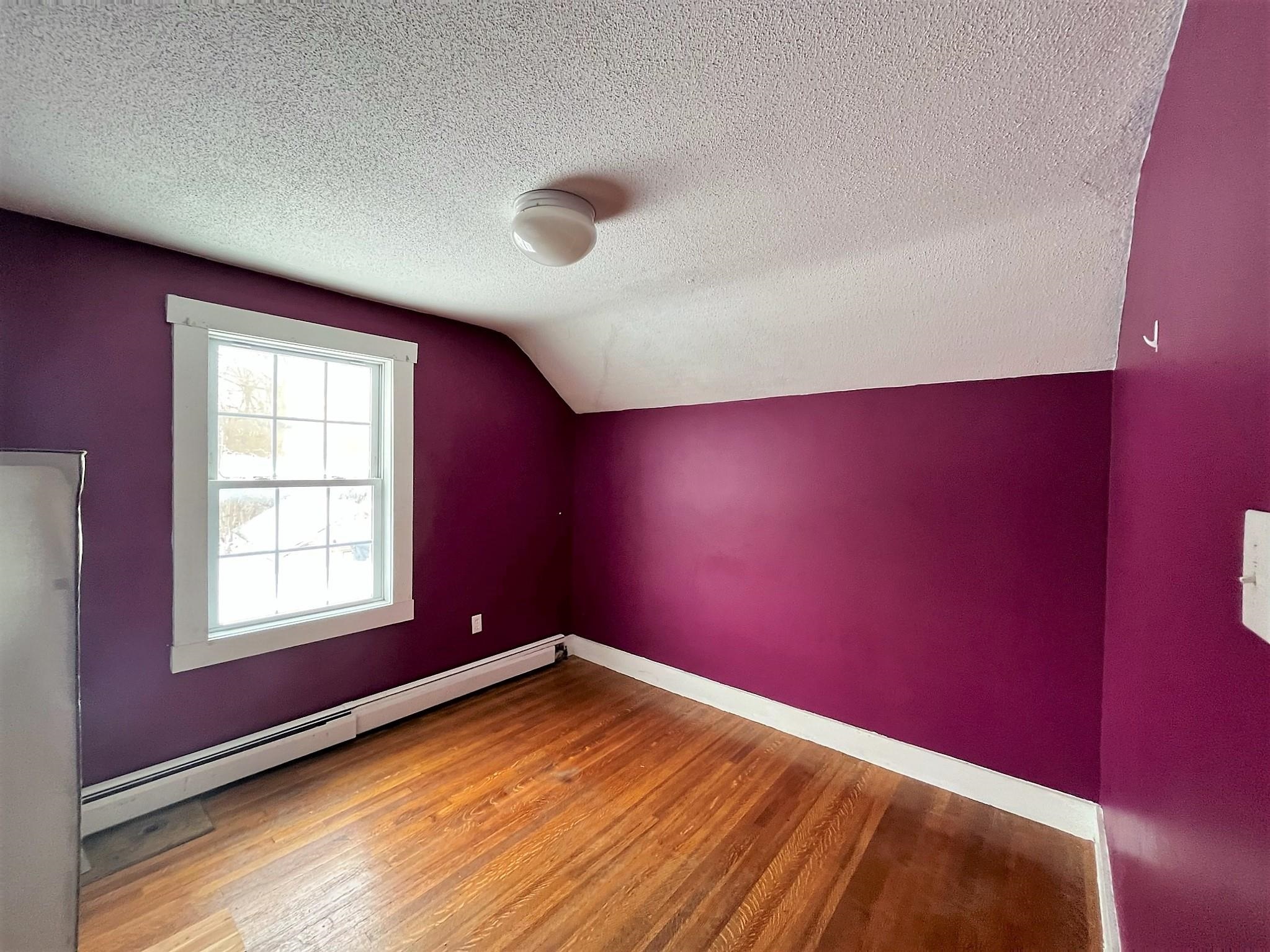 Empty room with purple walls, hardwood floors, and a sloped ceiling.
