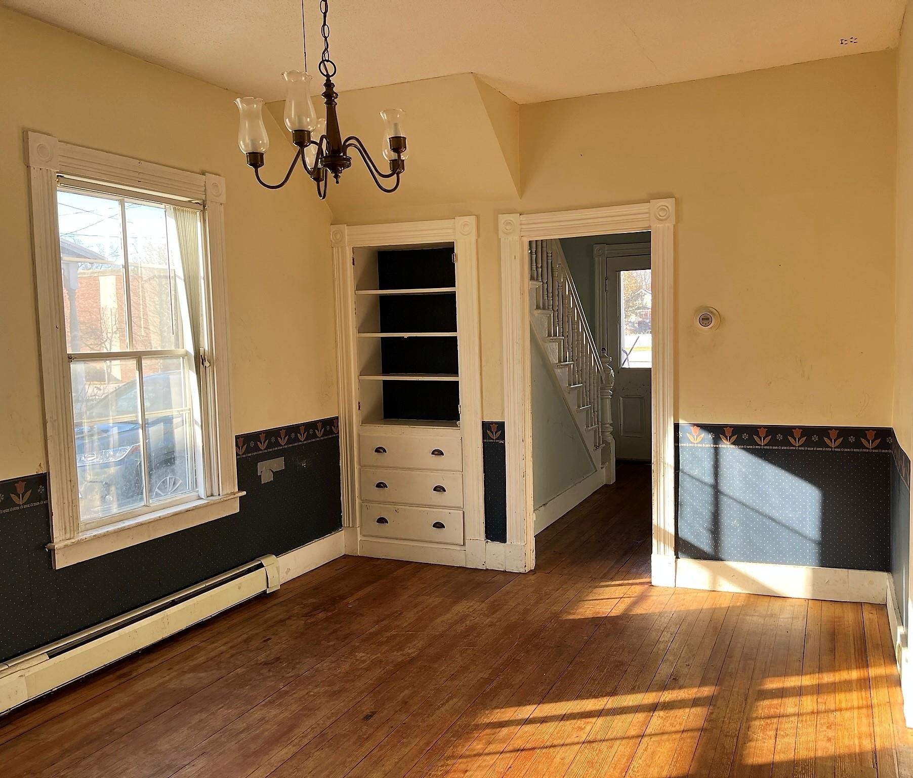 Empty room with hardwood floors, built-in shelving, decorative wainscoting, and sunlight across the floor.