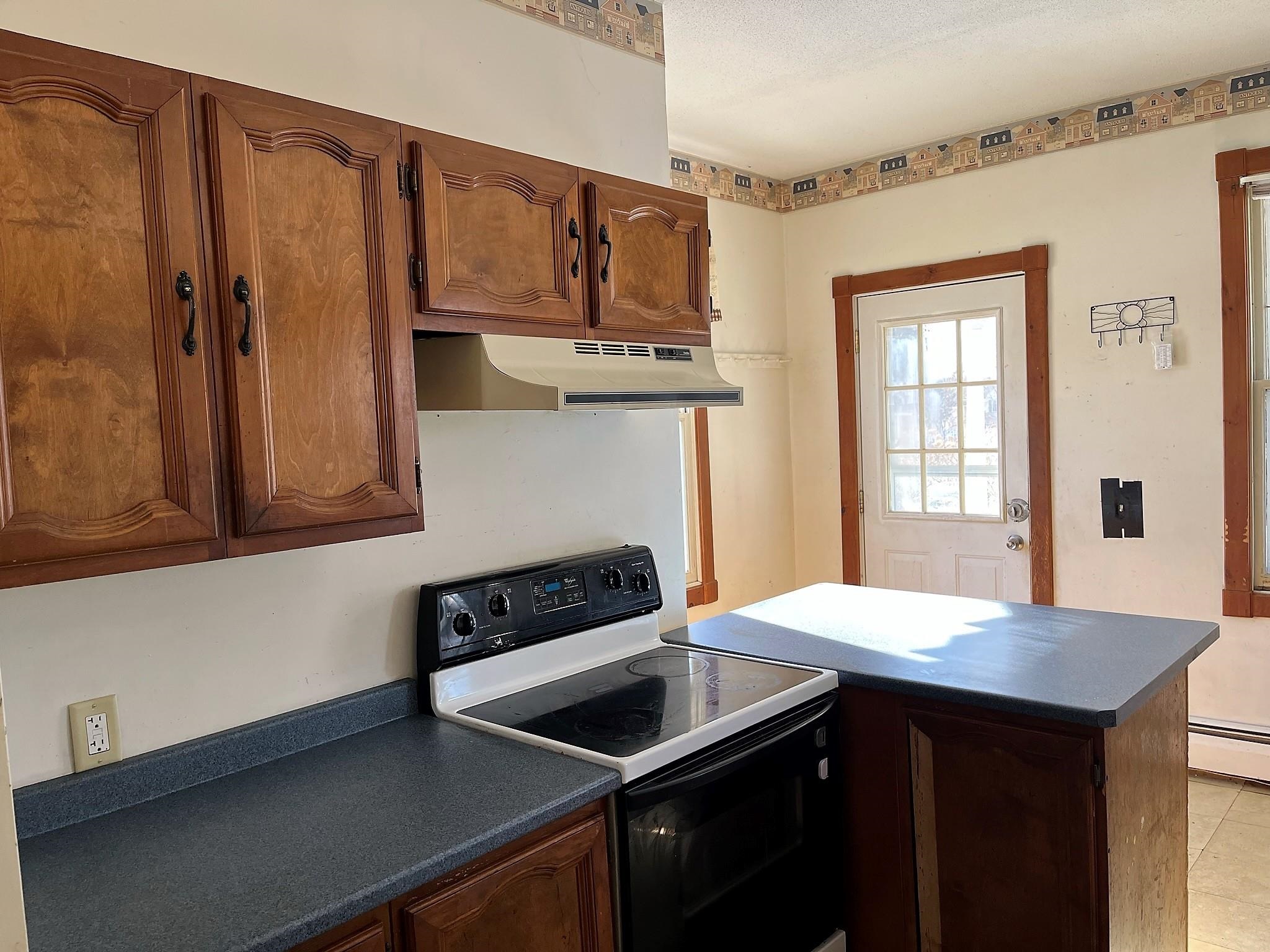 Kitchen with dark wood cabinets, blue-gray counters, an electric range, and a peninsula by the back door.