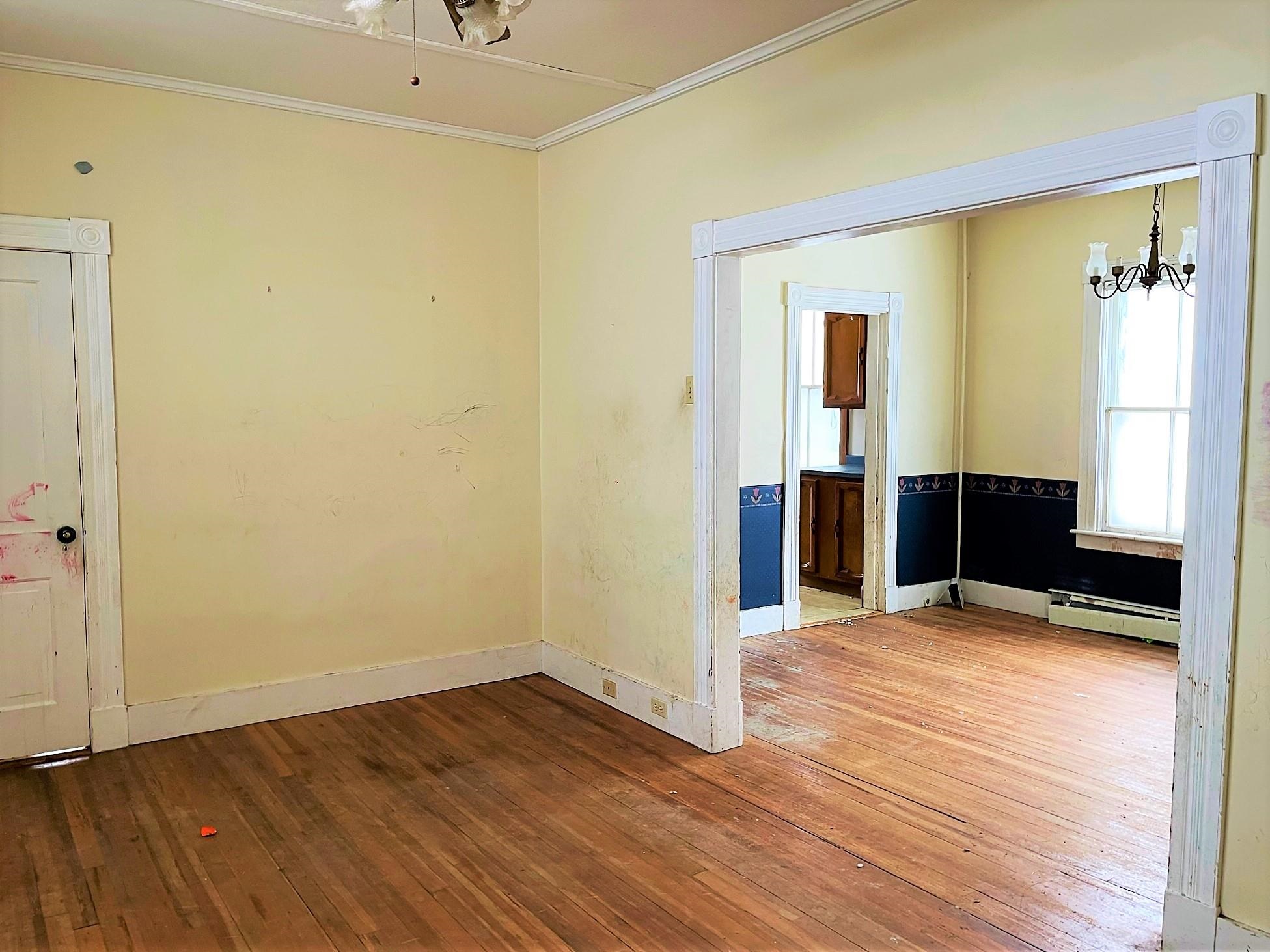 Vacant rooms with worn hardwood floors, ornate white trim, and dark wainscoting.