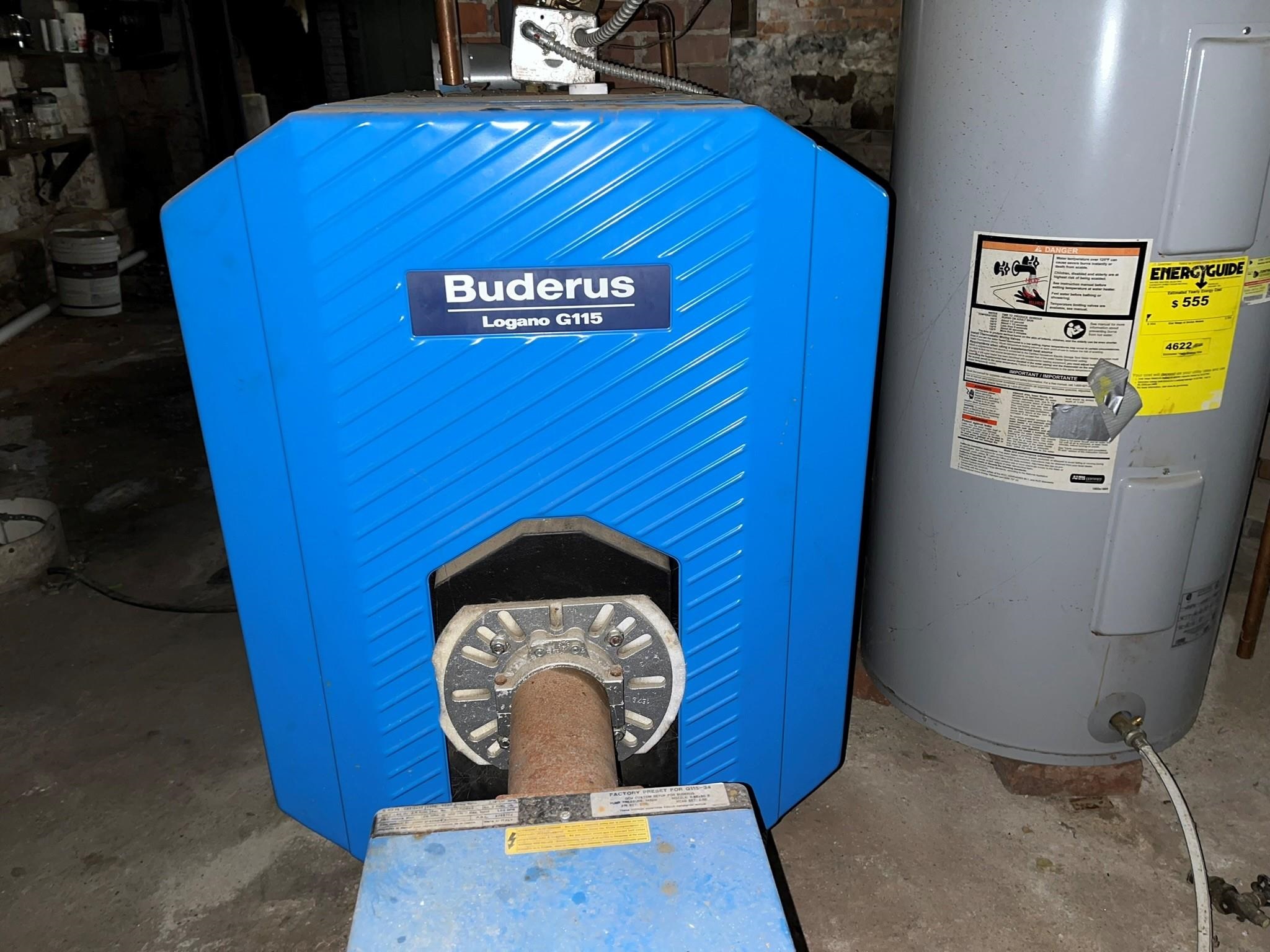 Blue Buderus boiler beside a gray hot water tank in a basement utility area.