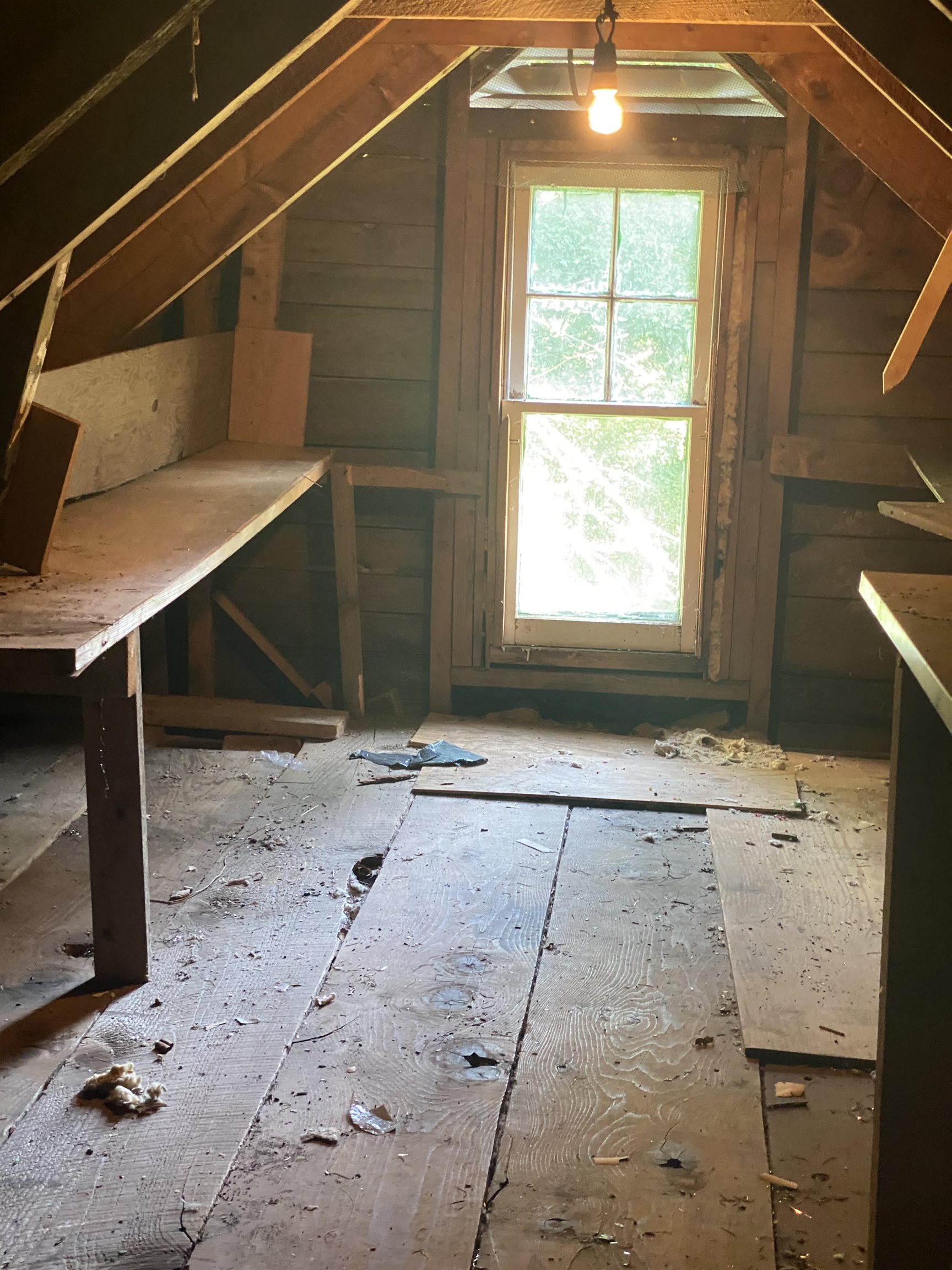 Unfinished attic with exposed rafters, rough plank floor, and a tall window.