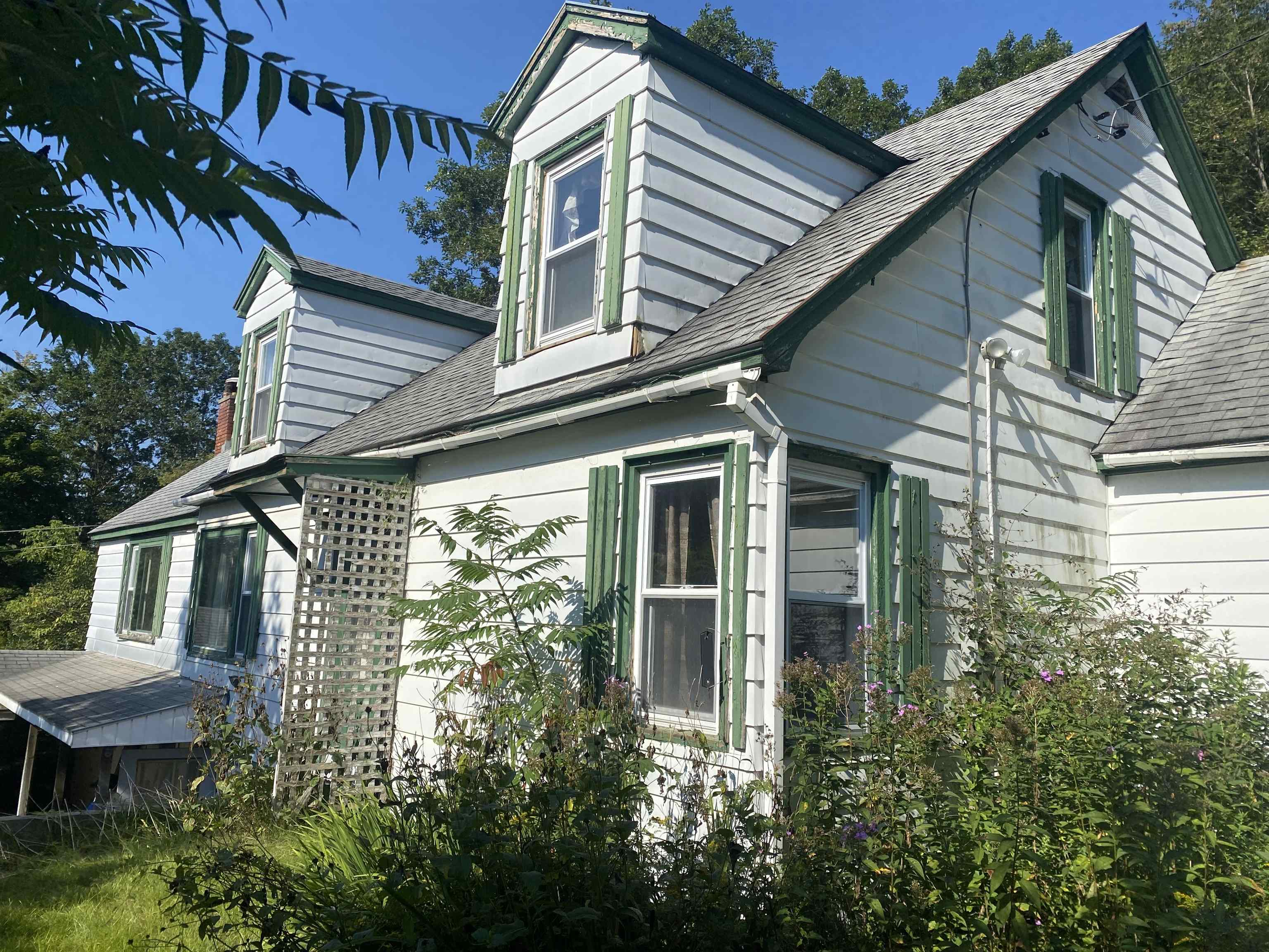 White clapboard house with green trim, steep gables, and flowering shrubs along the facade.