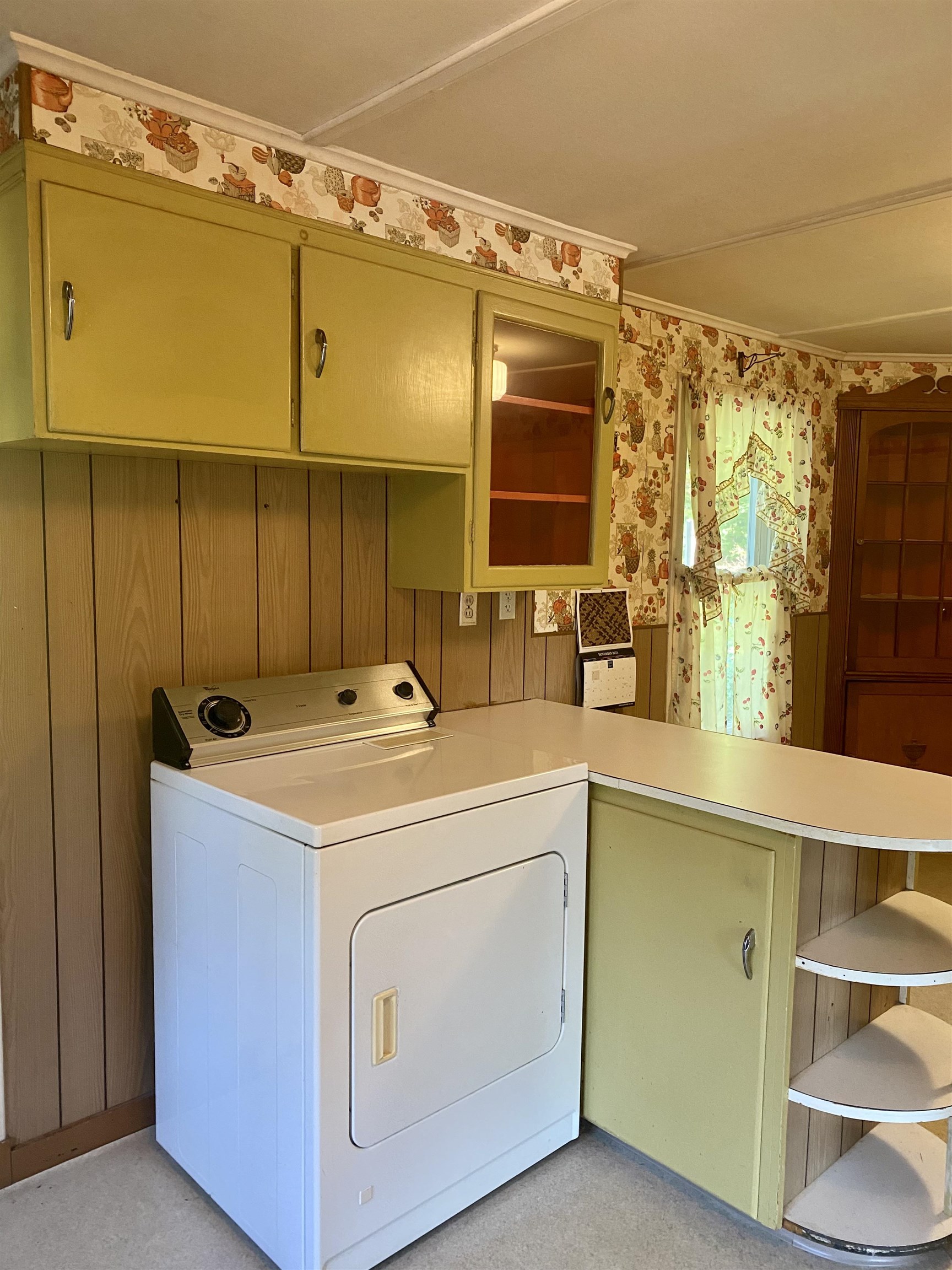 Laundry room with a white dryer, pale green cabinets, and floral curtains.