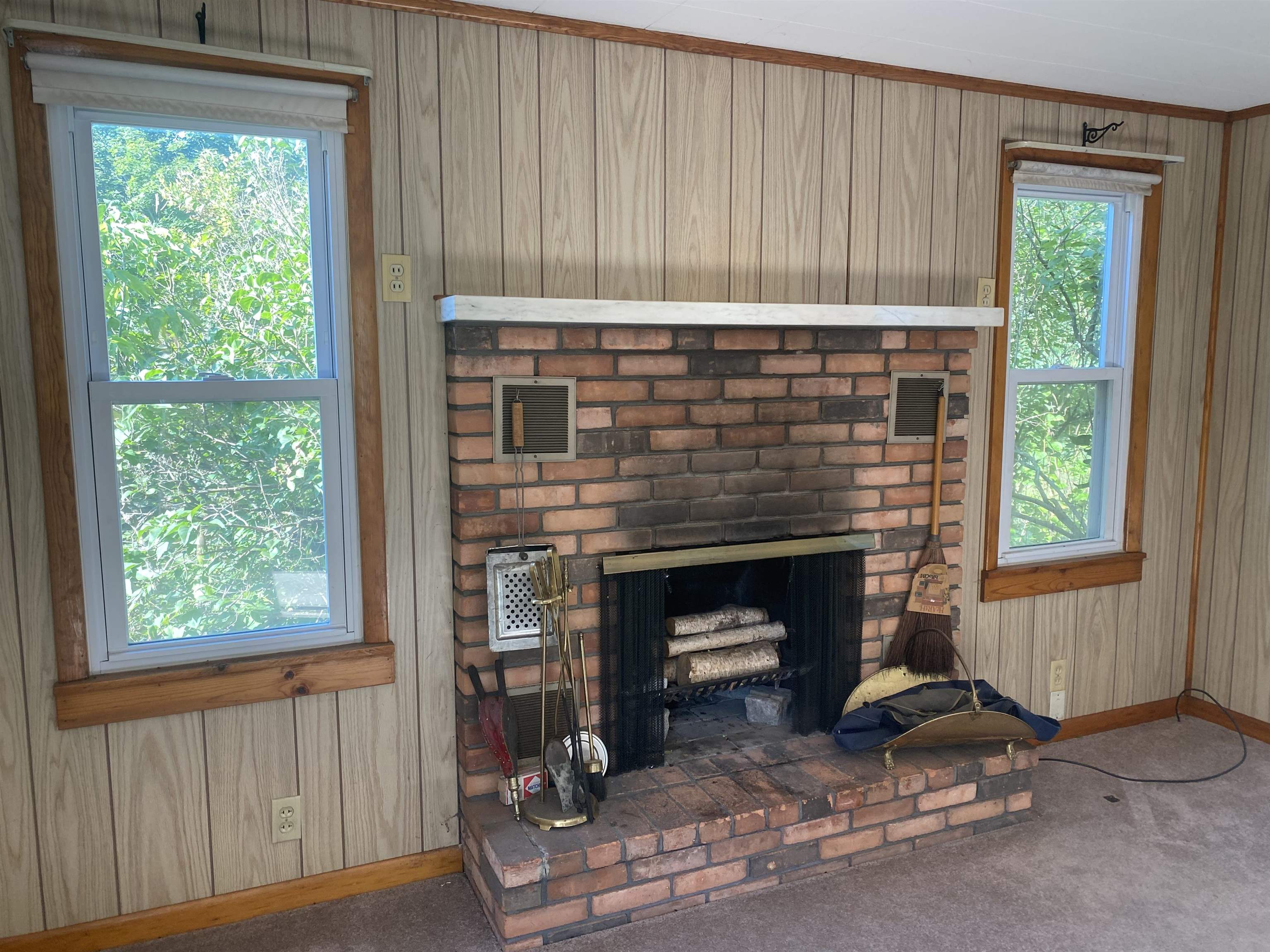 Brick fireplace and raised hearth between two windows in a wood-paneled room.
