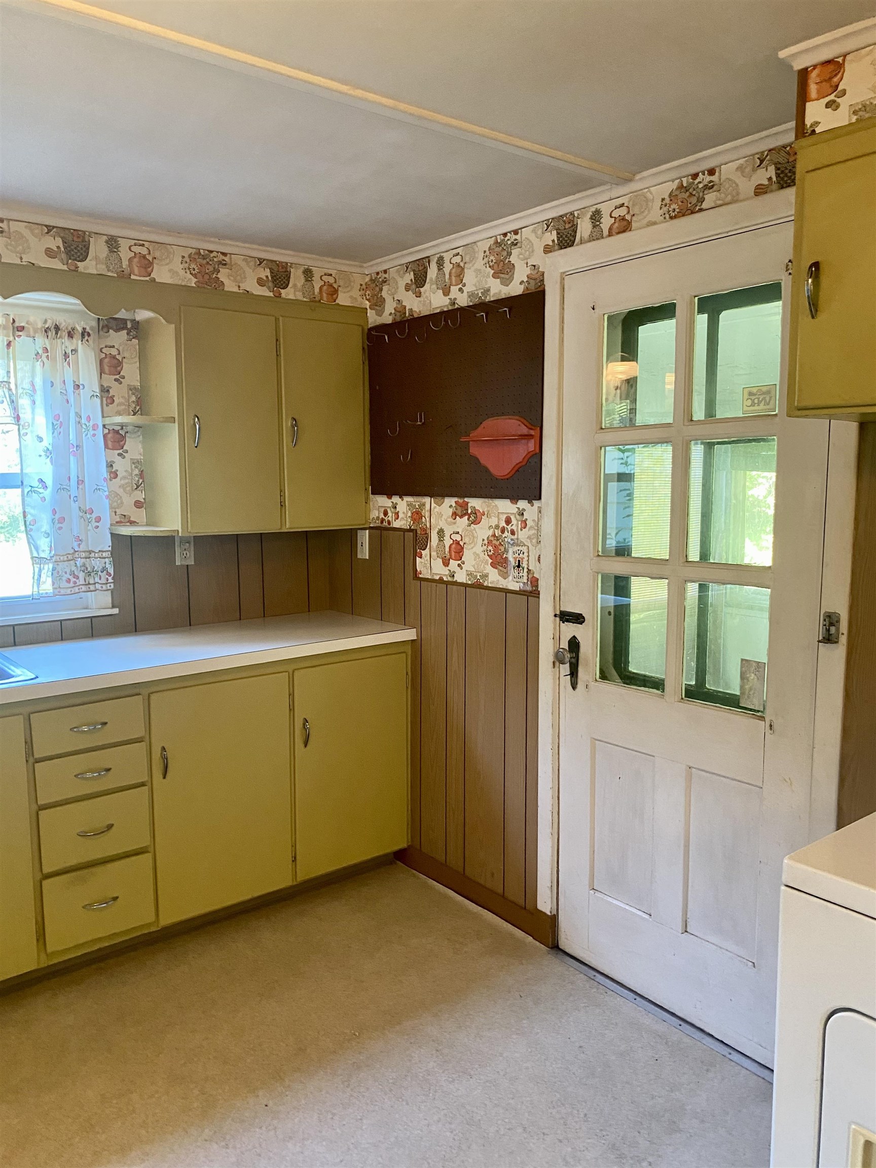 Kitchen with mustard-yellow cabinets, teapot-patterned wallpaper, and a glass-paneled door.