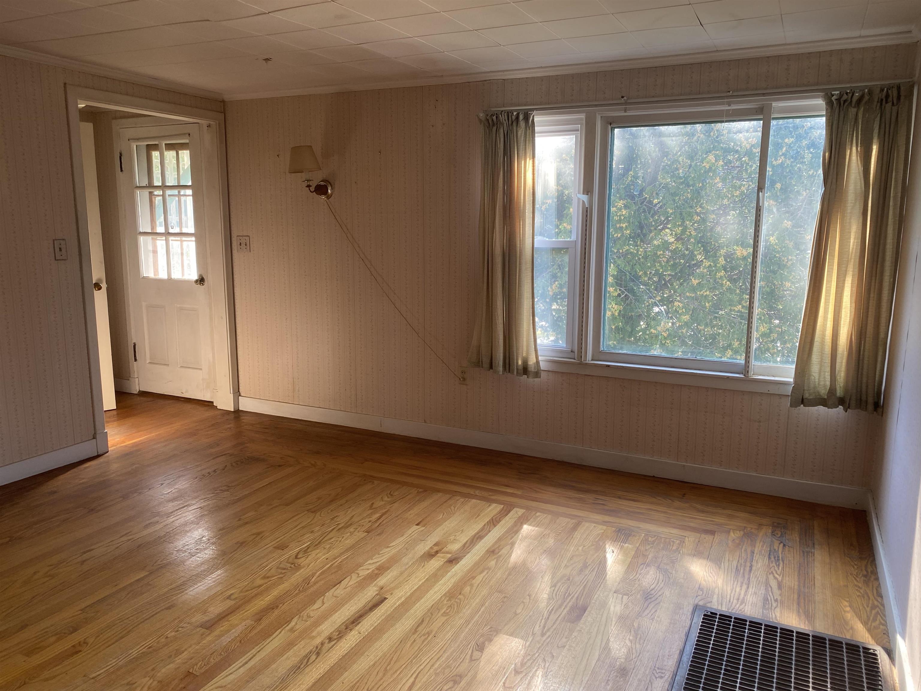 Empty room with polished hardwood floors, a large curtained window, and a doorway.
