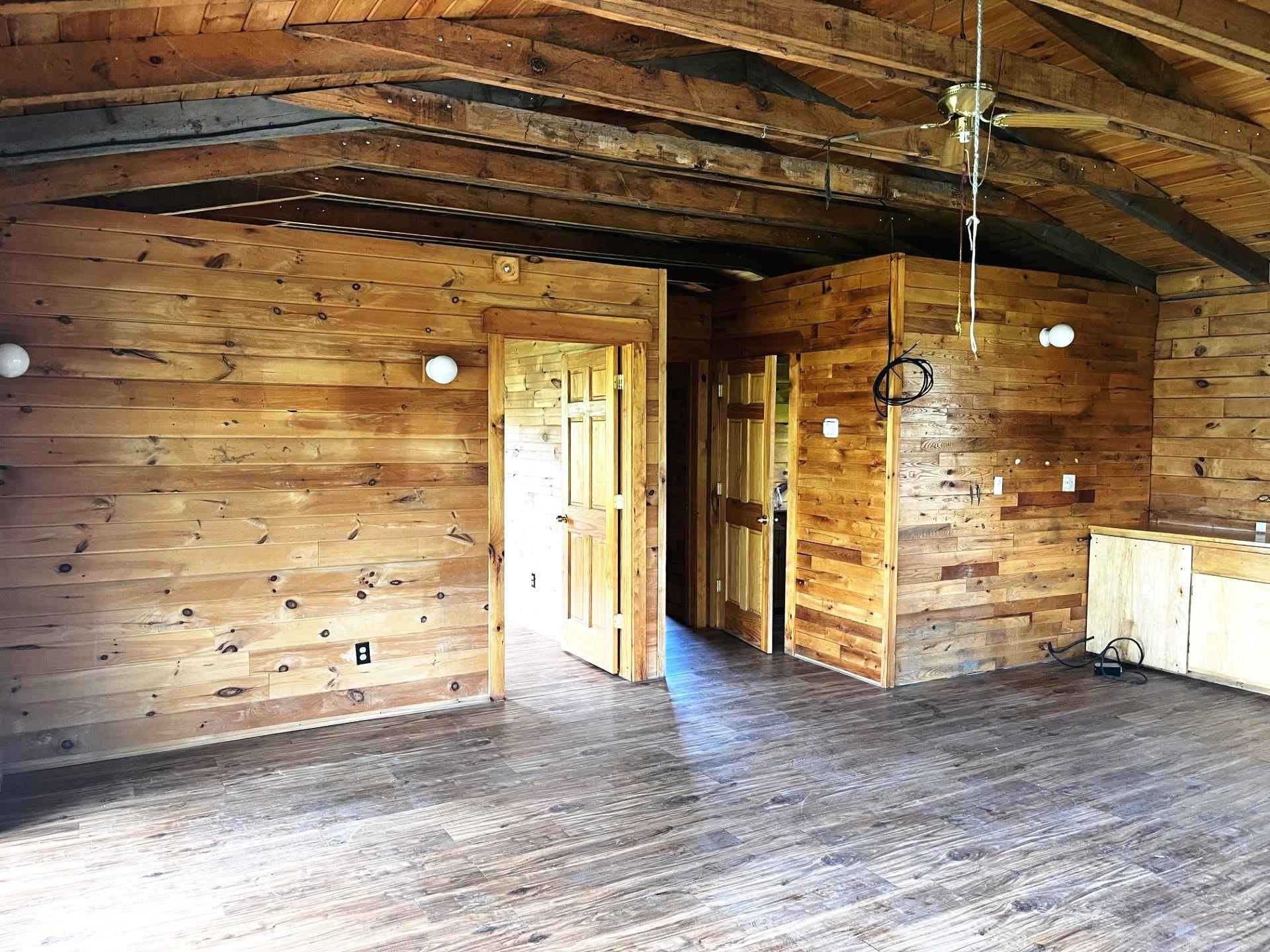 Vacant wood-paneled room with exposed ceiling beams, open doorways, and loose wiring.