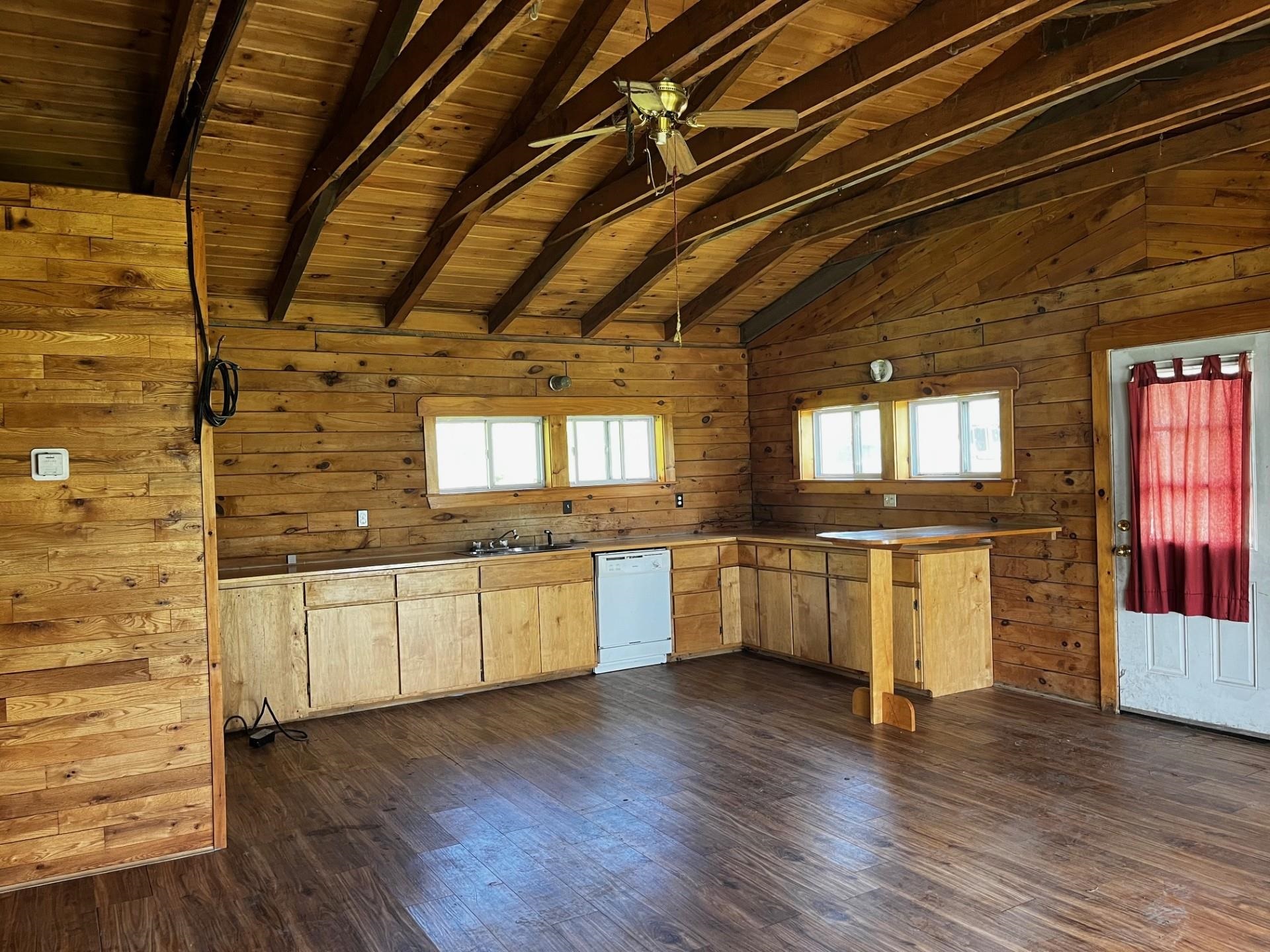Unfurnished wood-paneled kitchen with exposed beams, wooden cabinets, dishwasher, and red-curtained door.