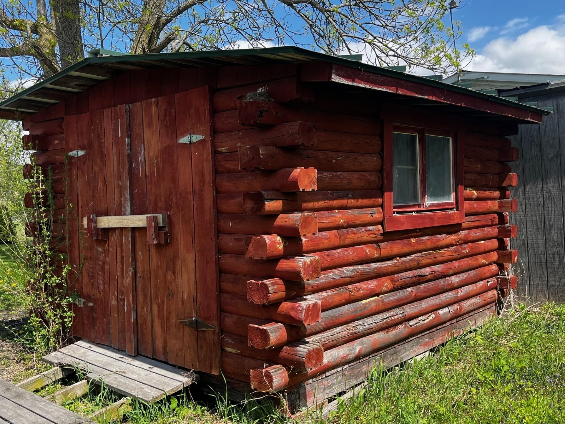 Weathered red log outbuilding with a wide wooden door and small window.