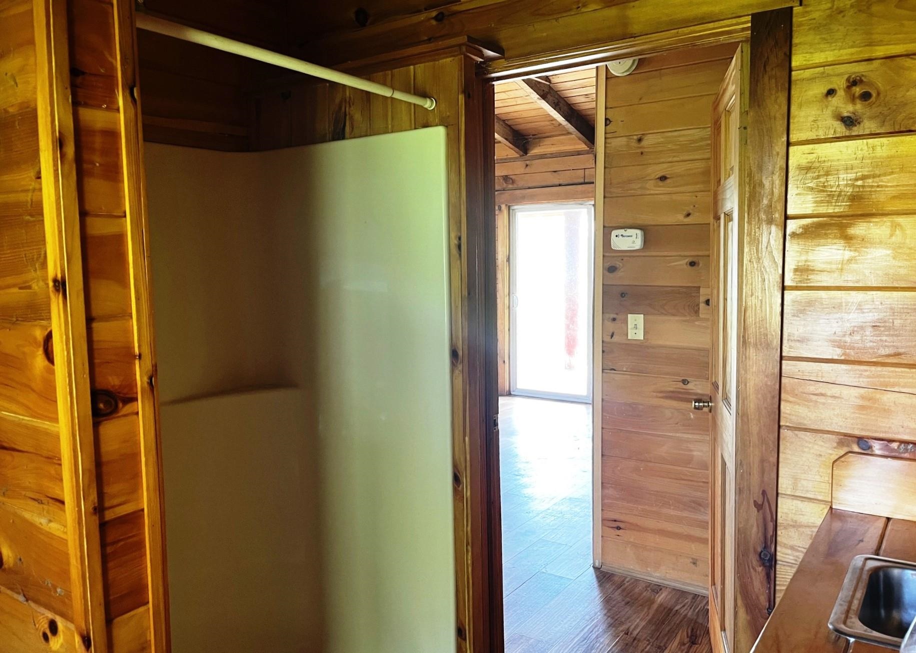 Wood-paneled kitchen with a large refrigerator and an open doorway to a bright adjoining room.