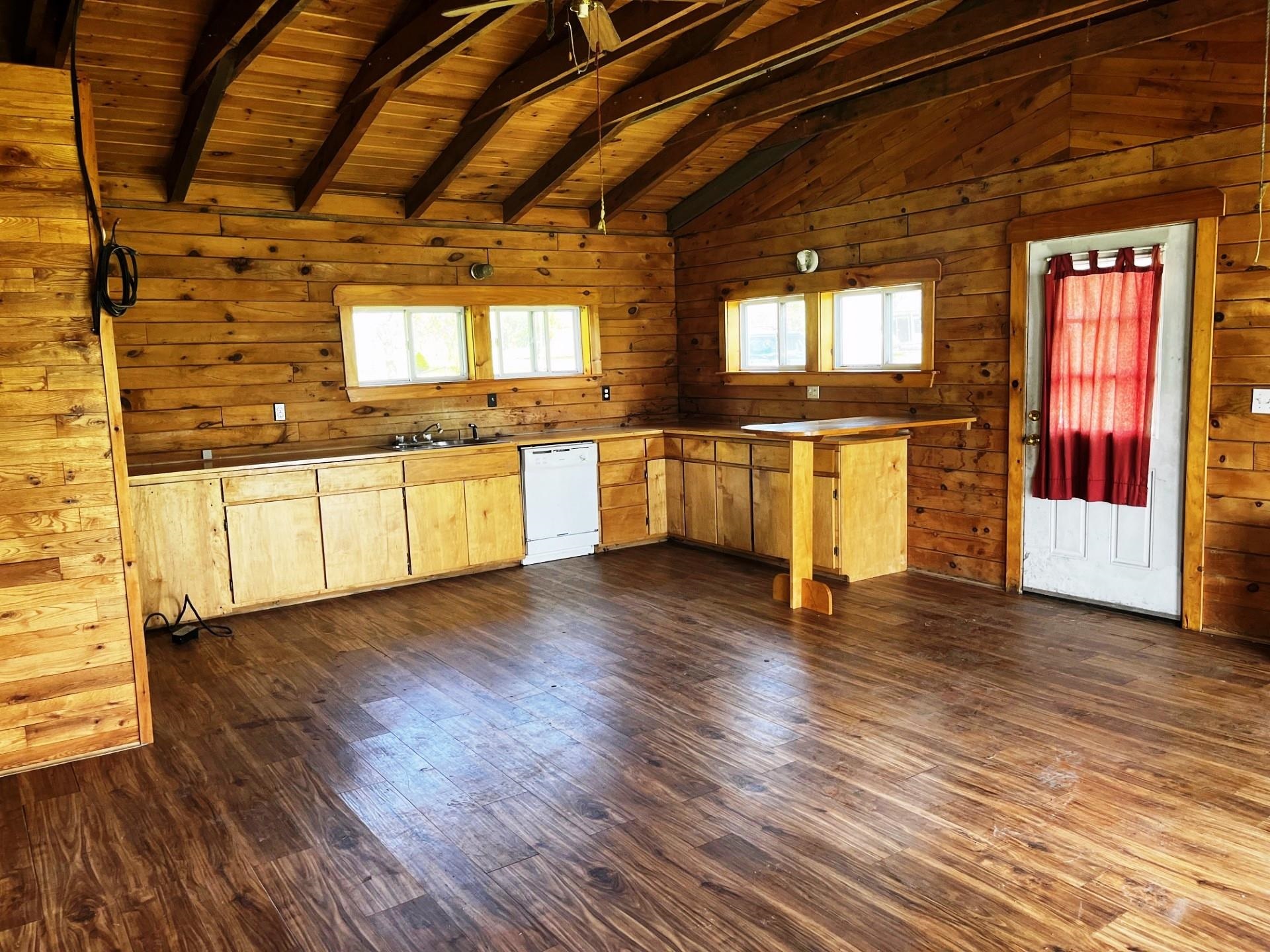 Wood-paneled kitchen with exposed beams, light cabinets, and a red-curtained door.