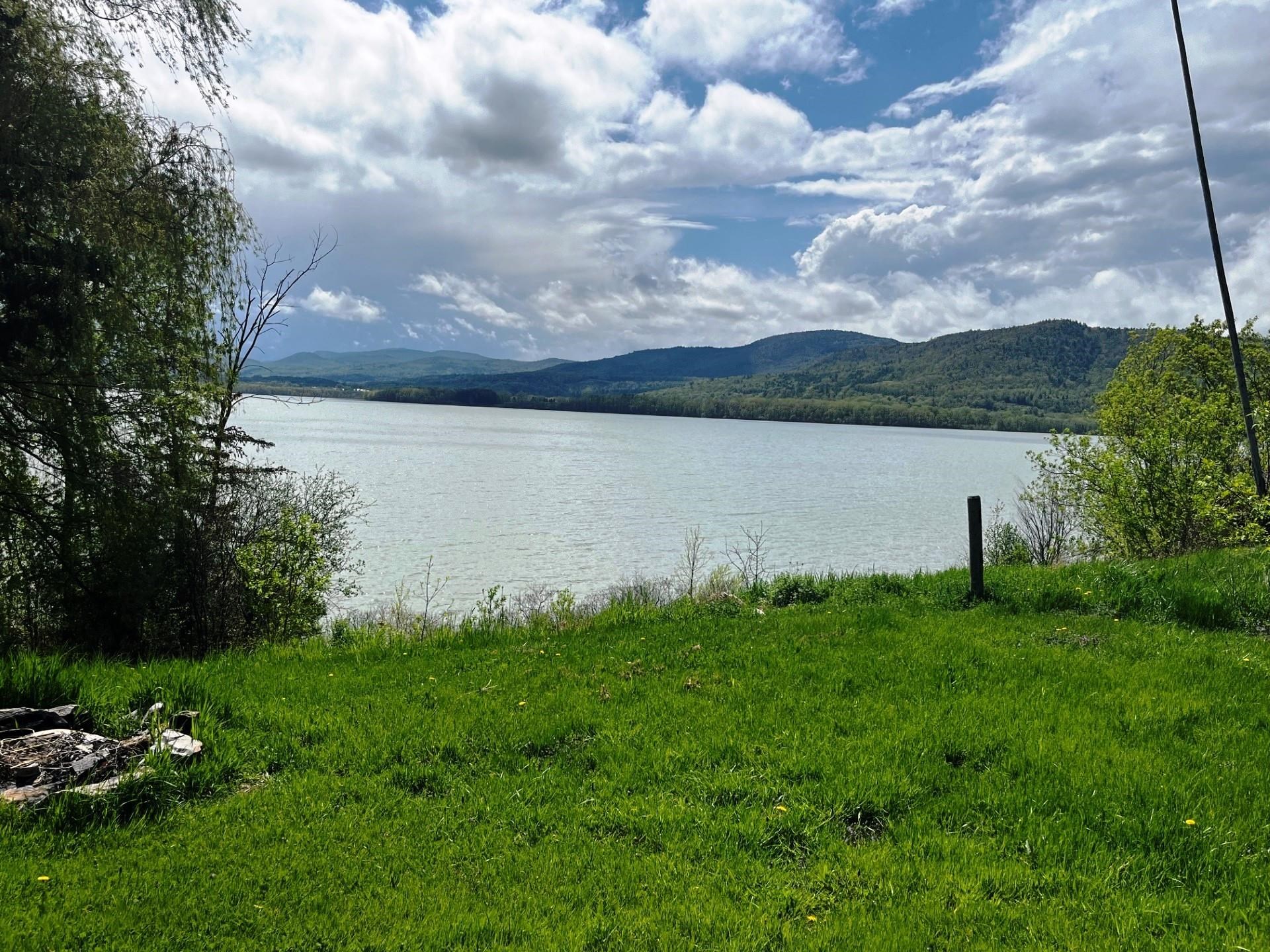 Lake and wooded mountains beyond a green grassy shoreline.