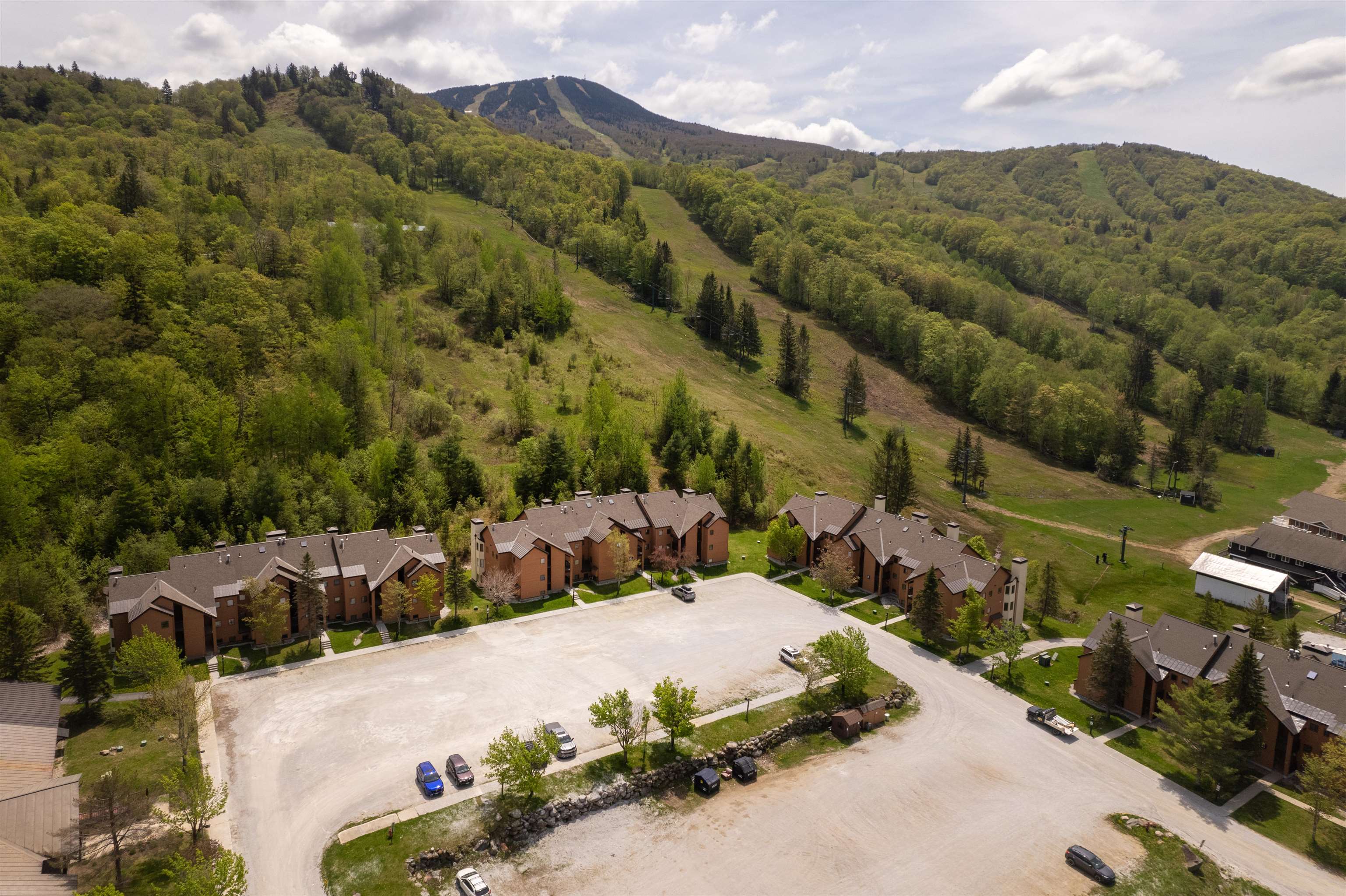 Aerial view of brick condominiums below a wooded mountain with a grassy ski trail.