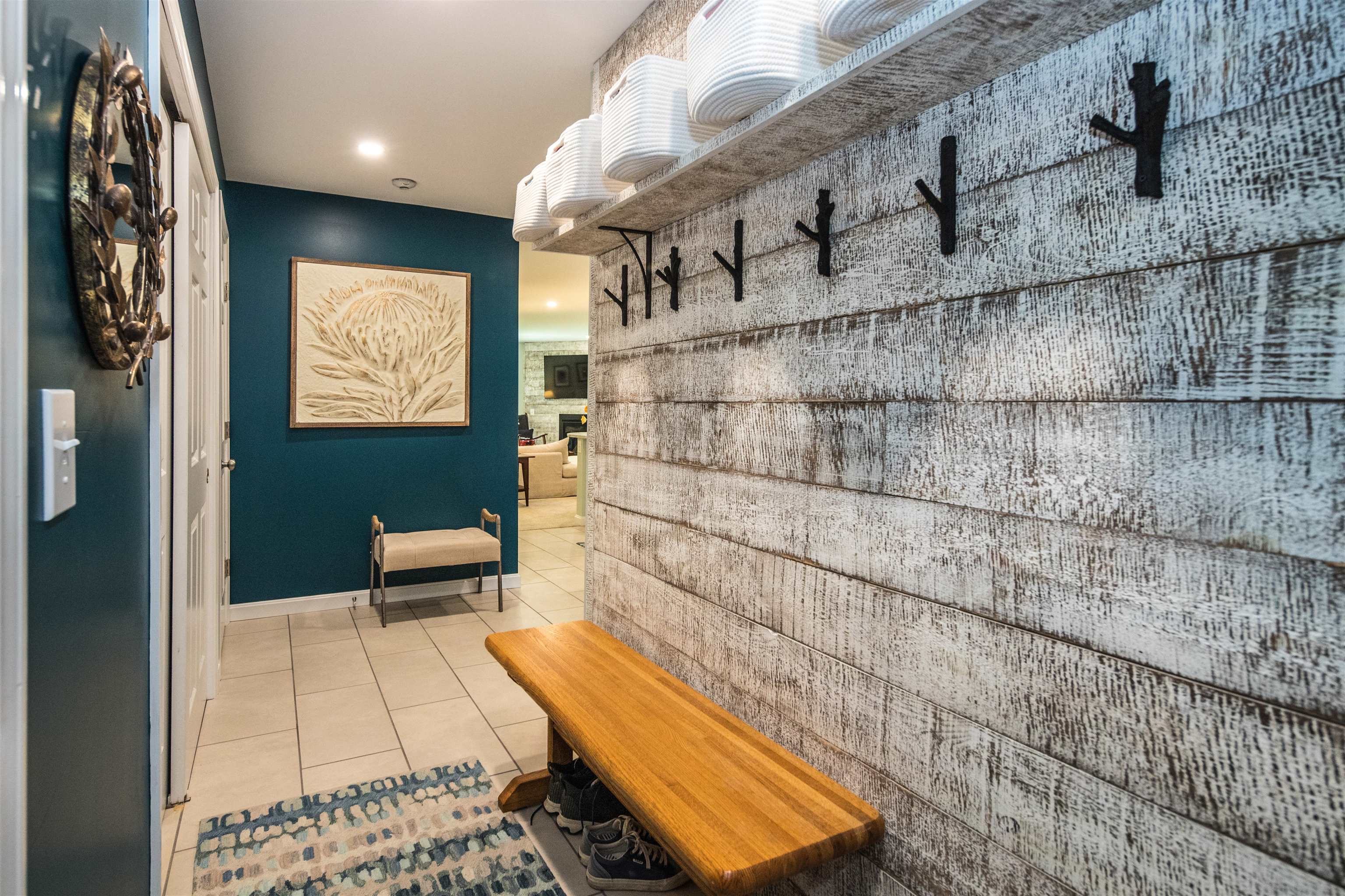Entryway with wooden bench, shoe storage, coat hooks, baskets, and a teal accent wall.