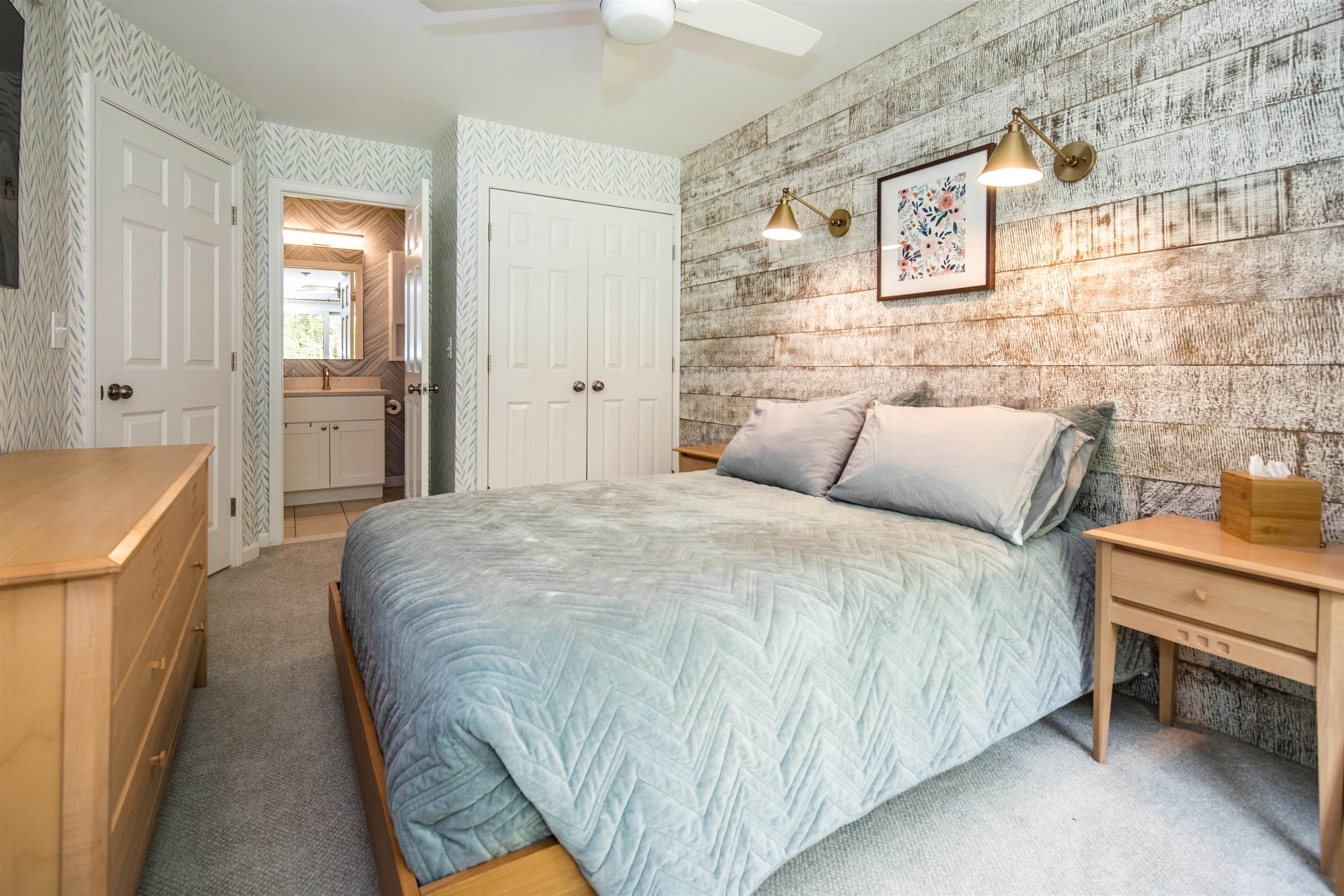 Bedroom with pale blue bedding, a weathered plank accent wall, and an open en suite bathroom doorway.
