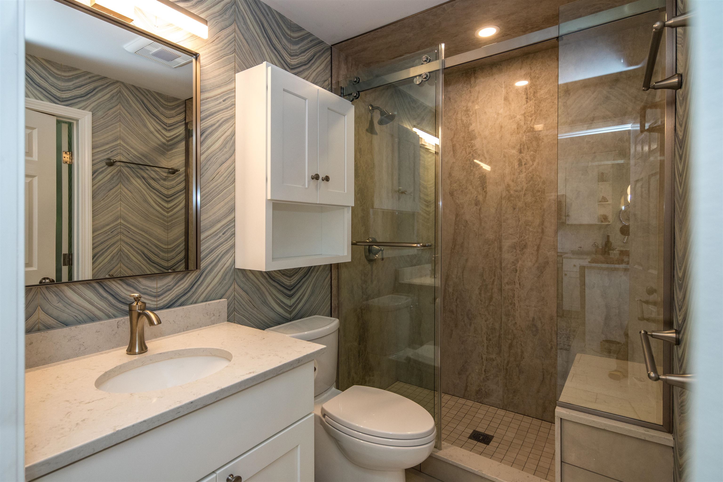 Bathroom with a white vanity, patterned gray tile, and a glass-enclosed walk-in shower.
