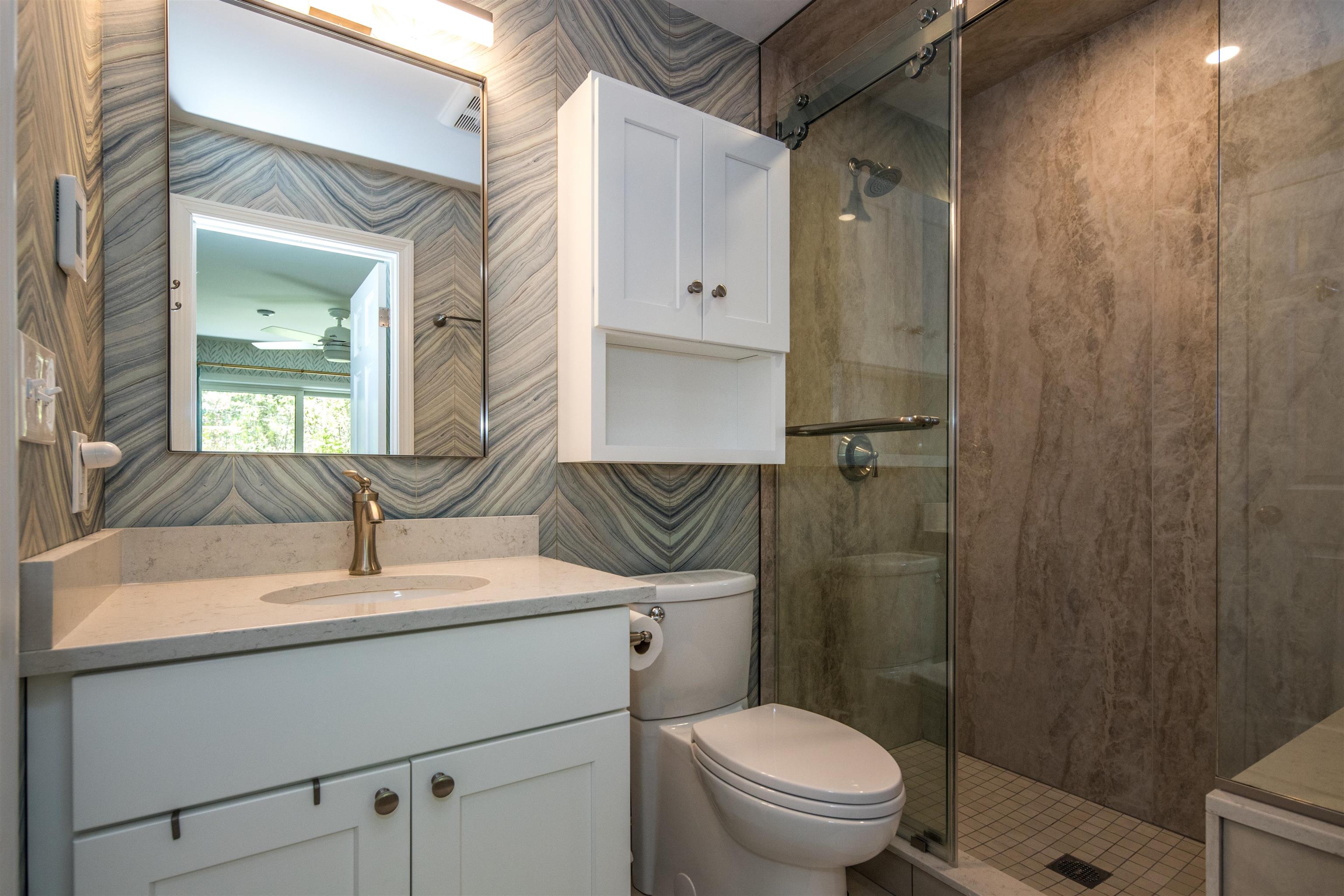 Bathroom with a white vanity, patterned gray walls, and glass-enclosed walk-in shower.