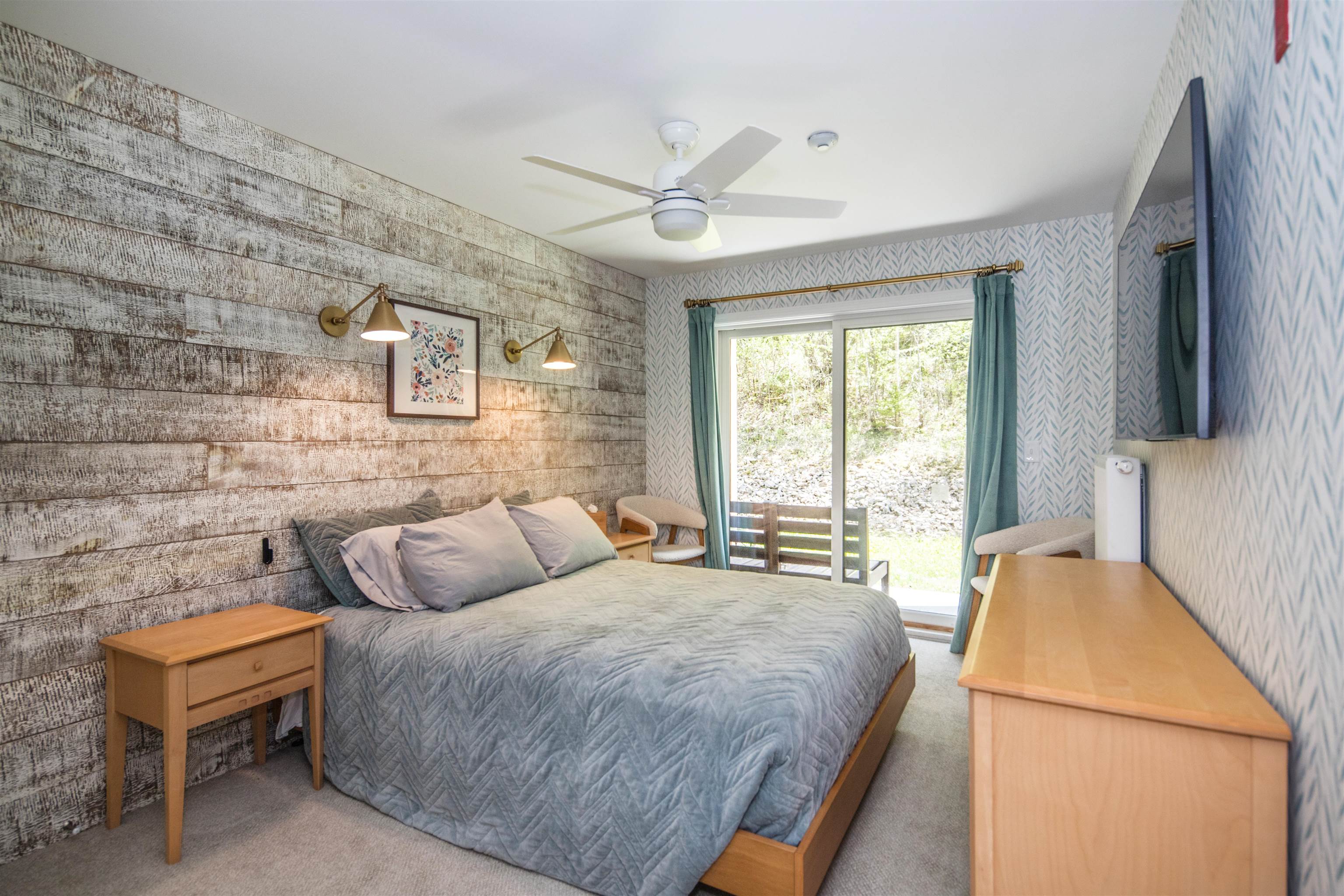 Furnished bedroom with a king-size bed, rustic accent wall, and sliding glass doors to the woods.