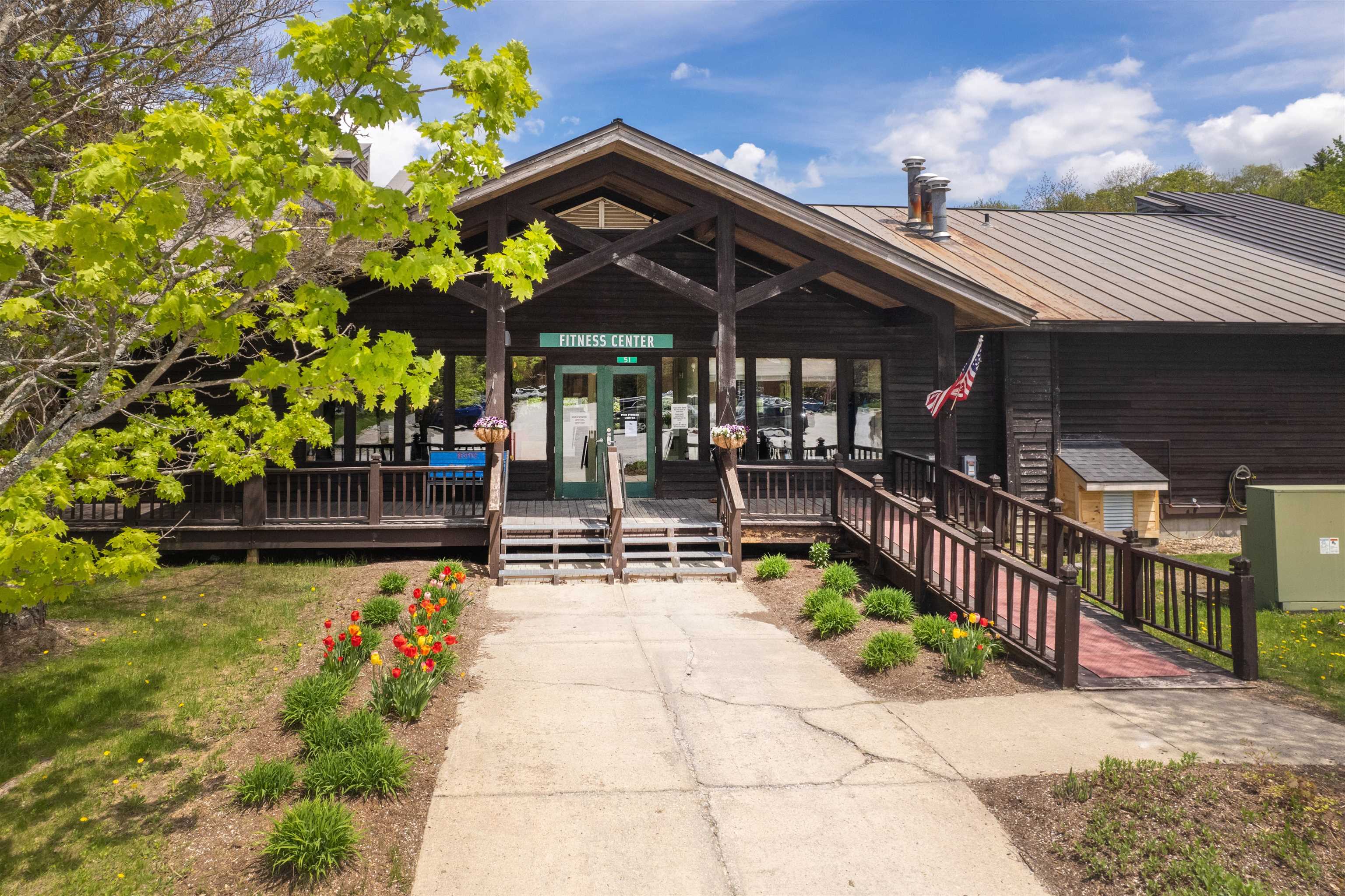 Timber fitness center building with a covered entrance, wooden ramp, and spring flower beds.