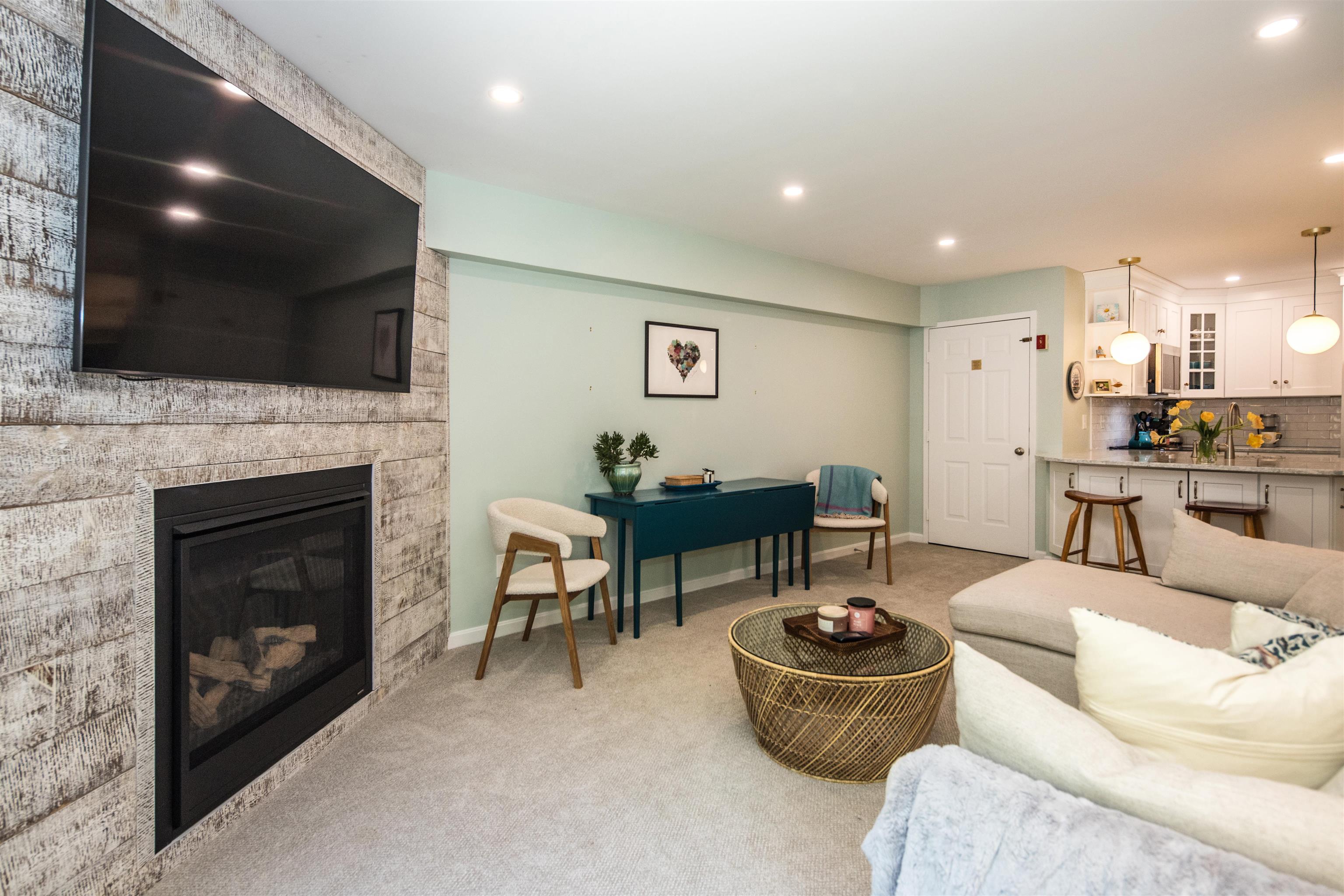 Living room with a fireplace and television beside an open kitchen and breakfast bar.