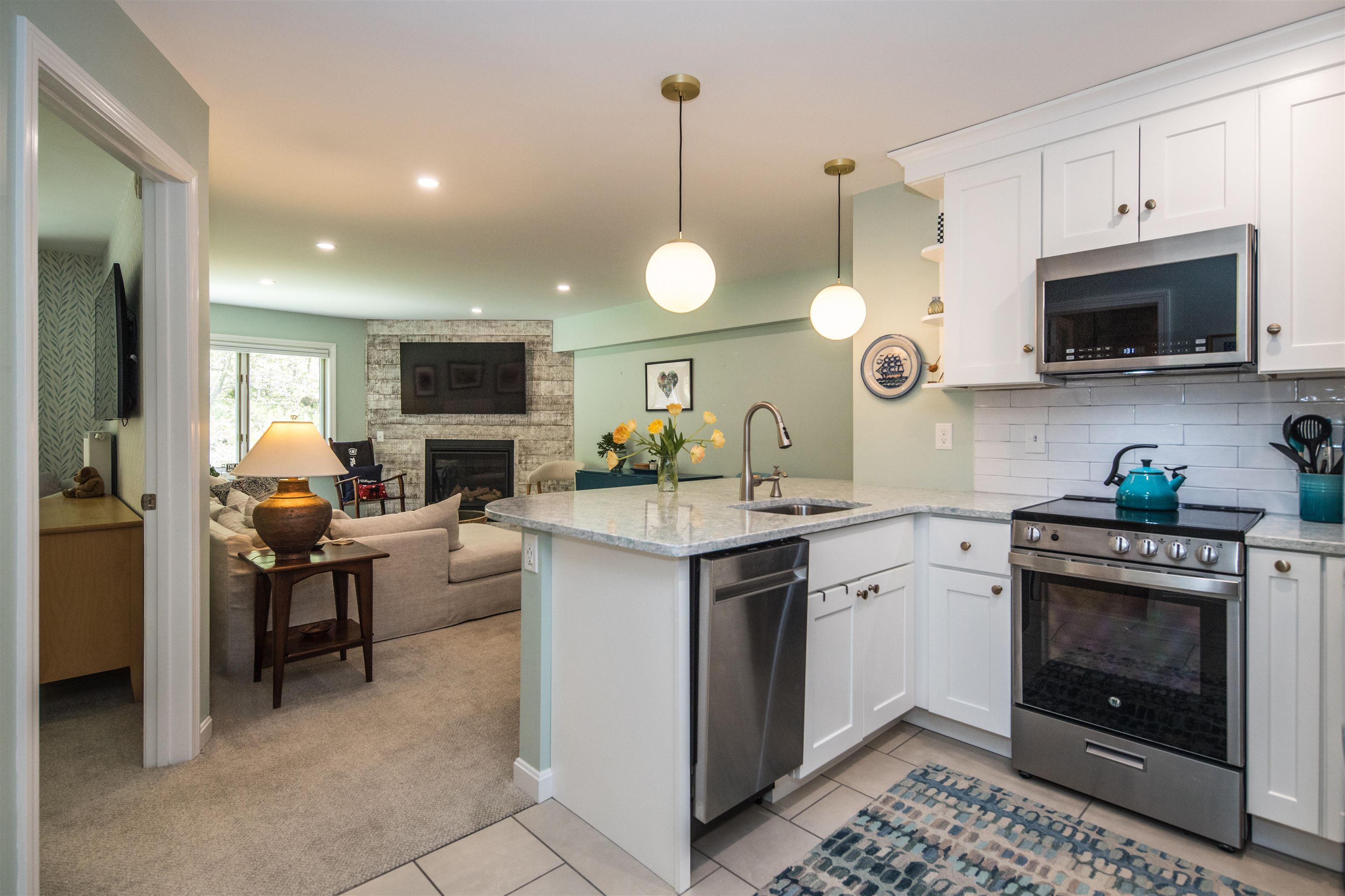 Open-plan kitchen and living room with white cabinets, stainless appliances, and a stone fireplace.