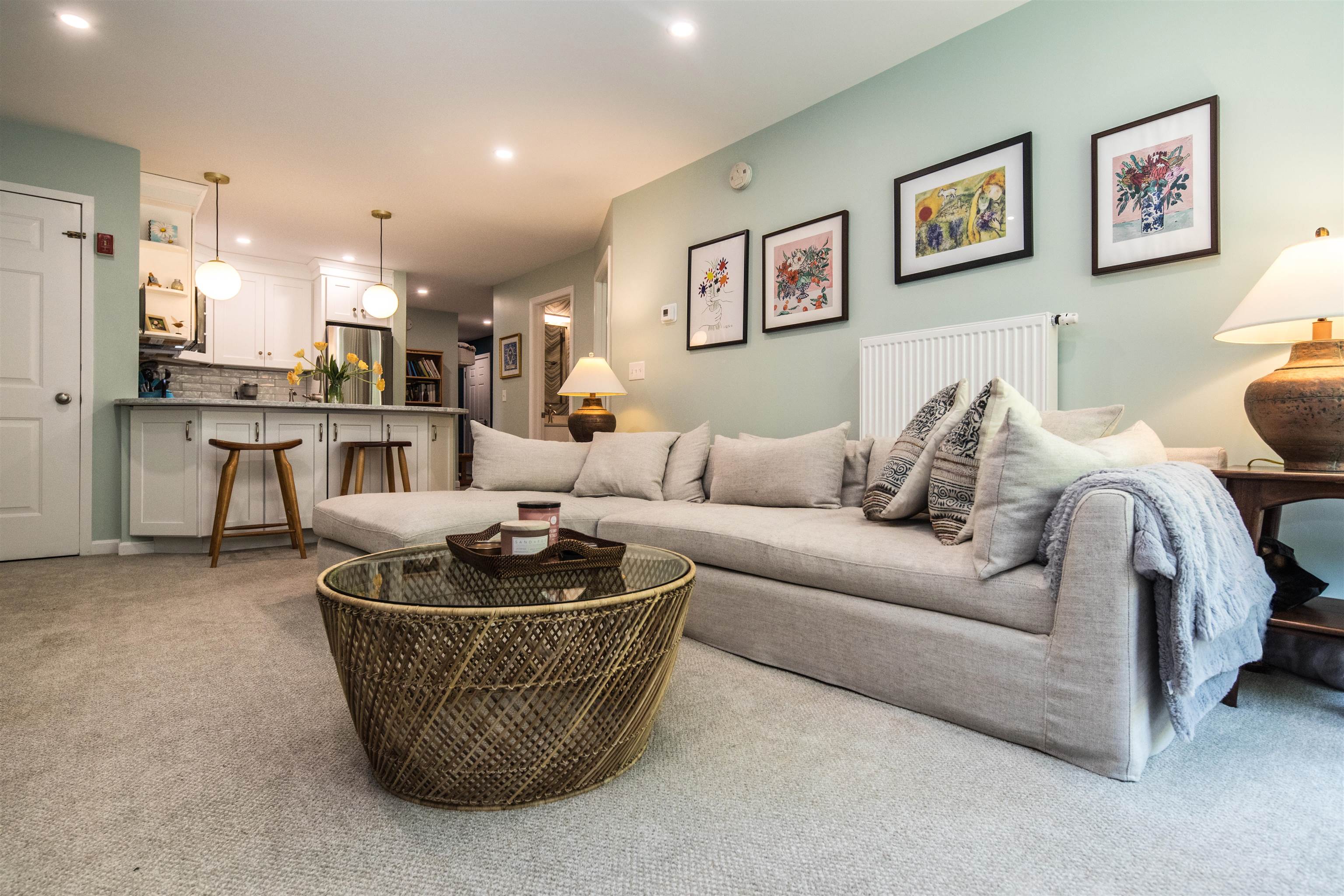 Furnished living room with a large gray sectional, woven coffee table, and open kitchen.