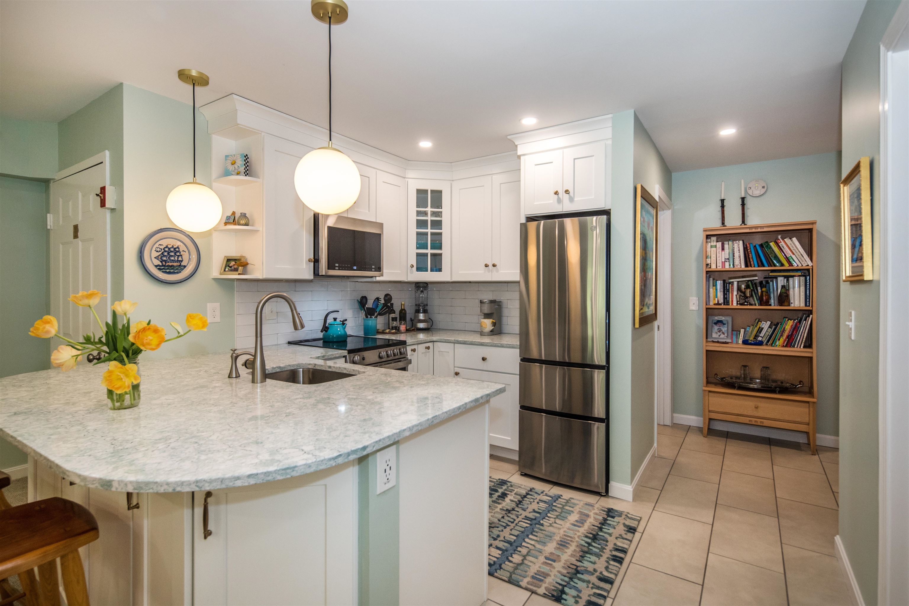 Kitchen with a large stone island, white cabinets, stainless steel appliances, and adjoining bookshelf.