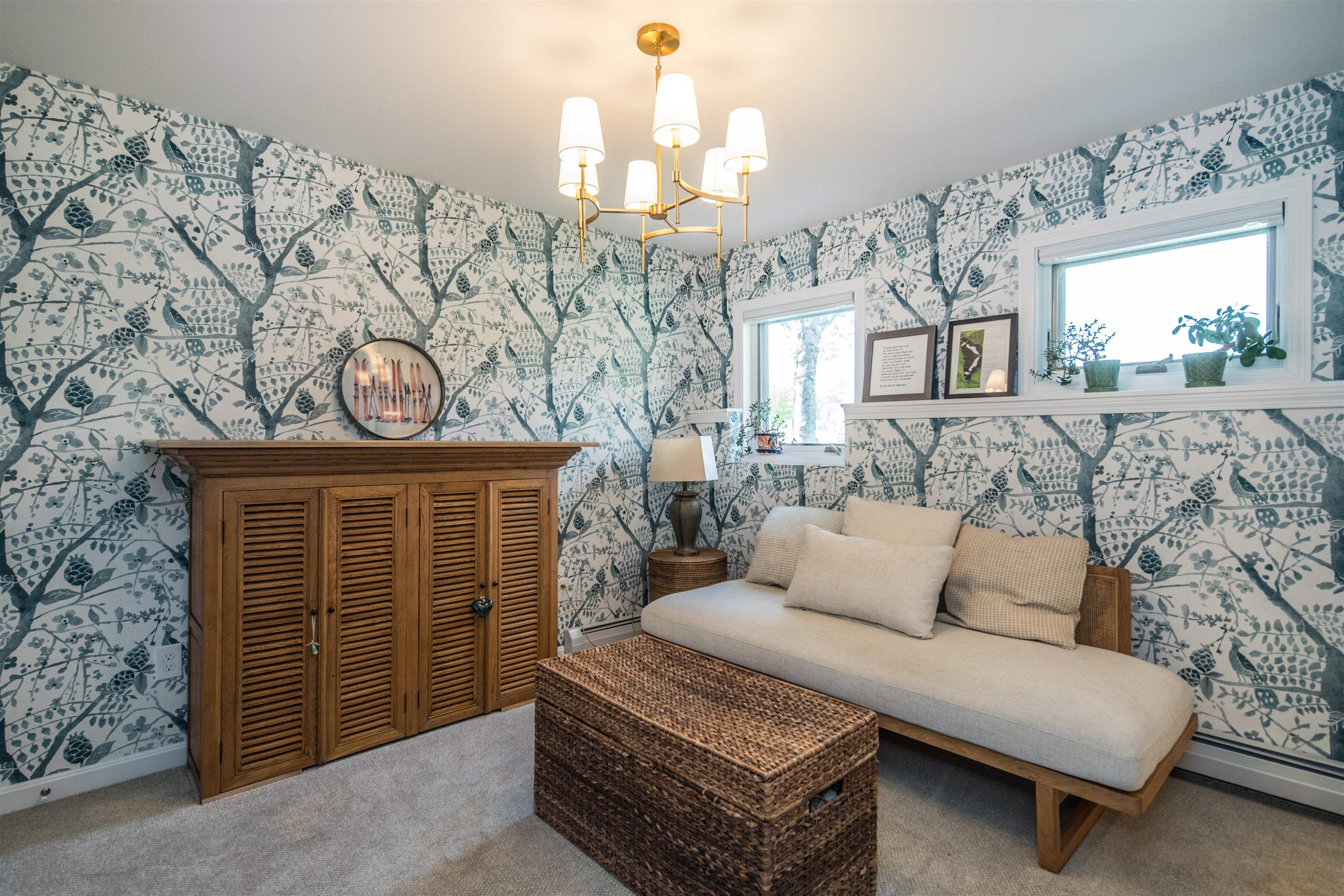 Sitting area with a cream chaise, woven coffee table, wooden cabinet, and botanical wallpaper.