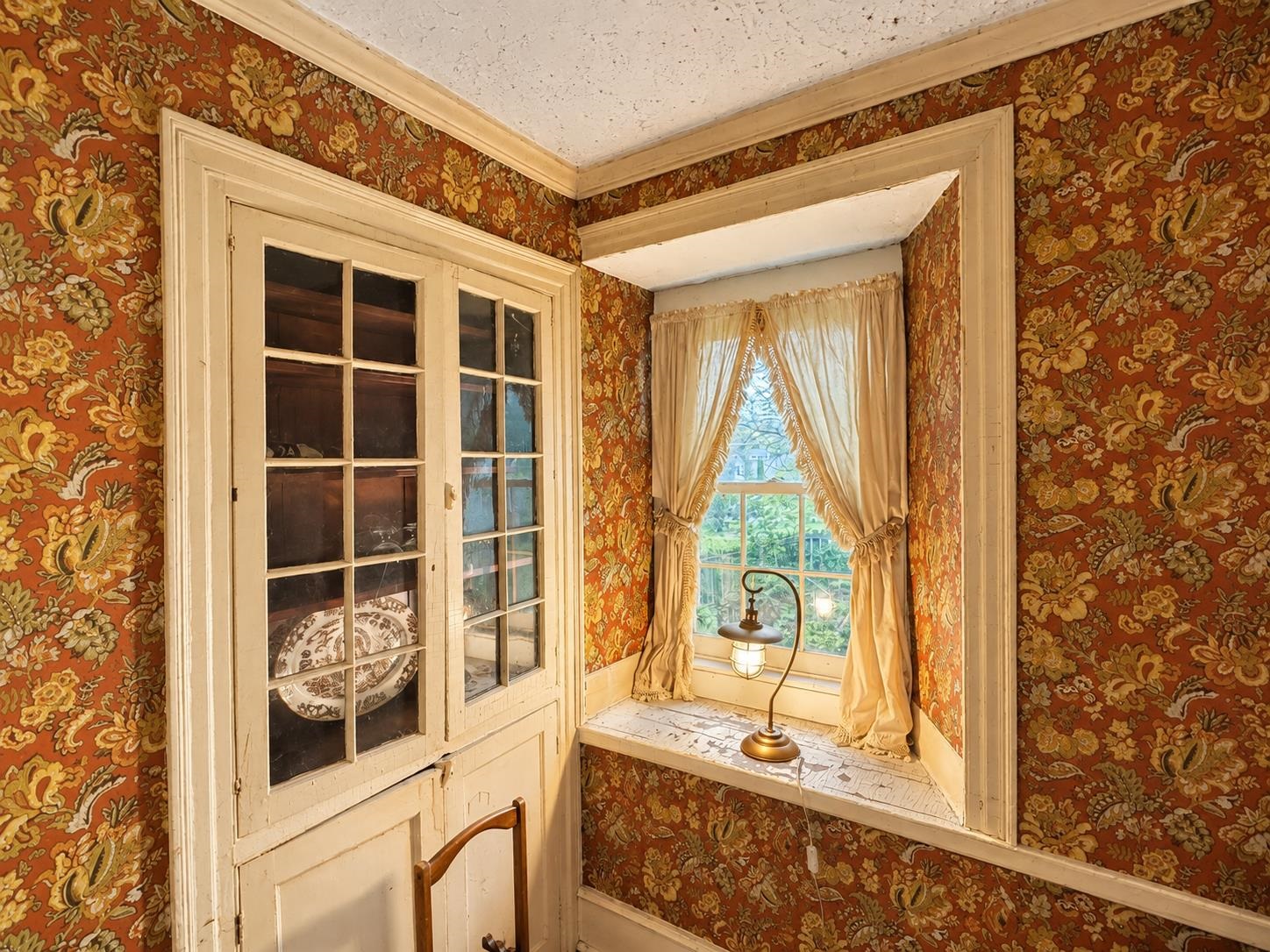 Floral-wallpapered nook with cream built-in cabinets, a curtained window, and a tiled window seat.