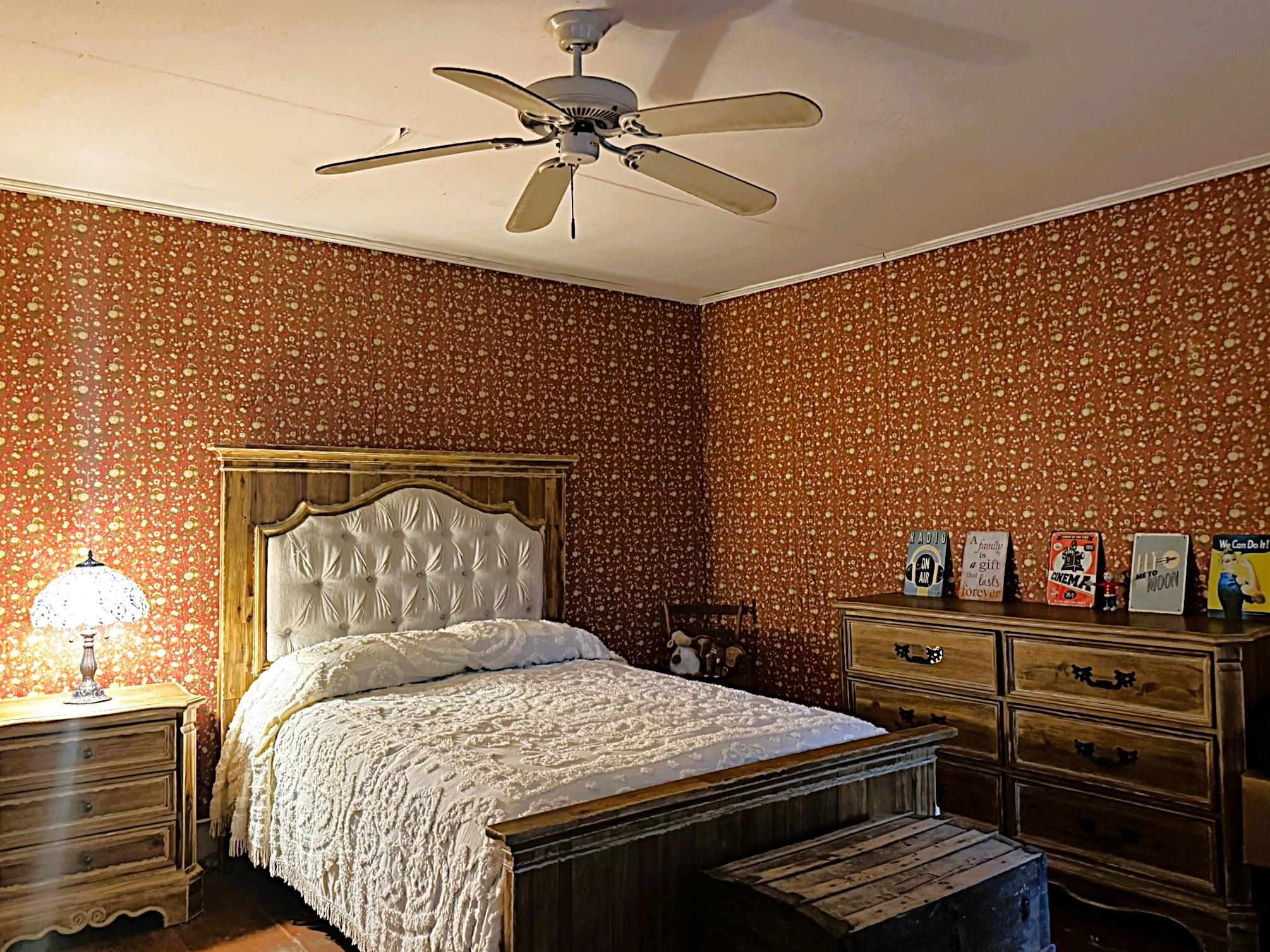 Furnished bedroom with a wooden bed, tufted cream headboard, and red floral wallpaper.