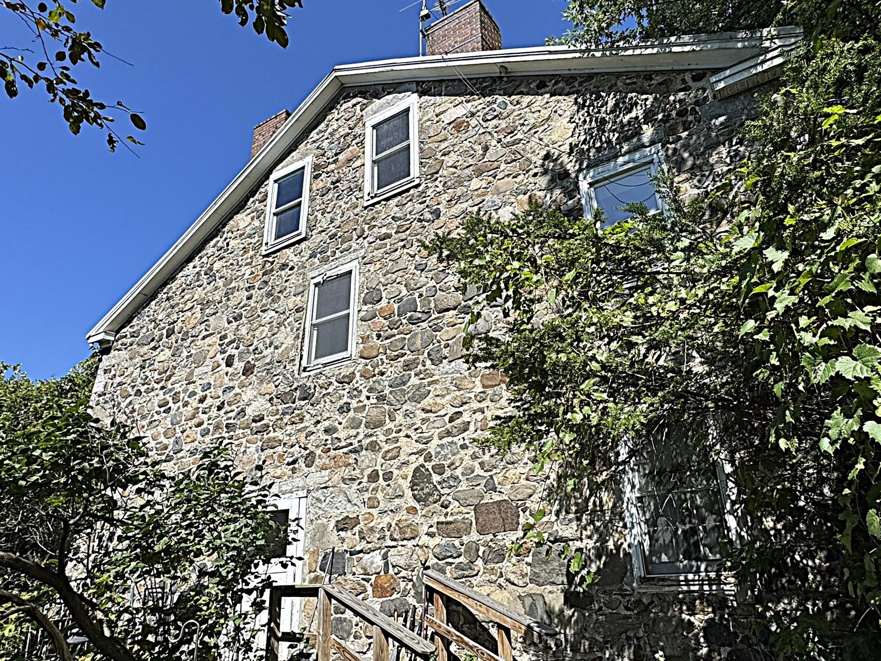 Stone house exterior with white-trimmed windows and a wooden entry stair among leafy trees.