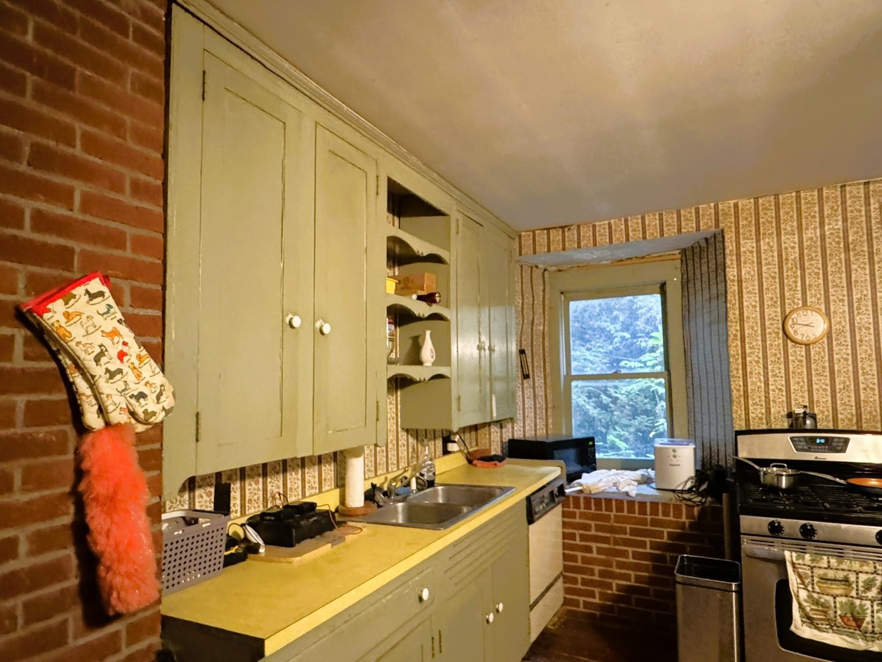 Kitchen with pale green cabinets, yellow counters, brick accents, and a stainless-steel range.