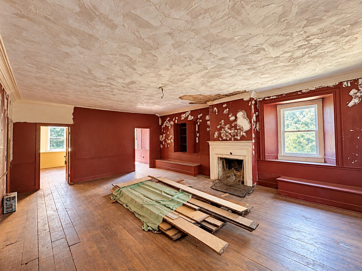 Vacant room with peeling red walls, a white fireplace, and removed floorboards piled on the floor.