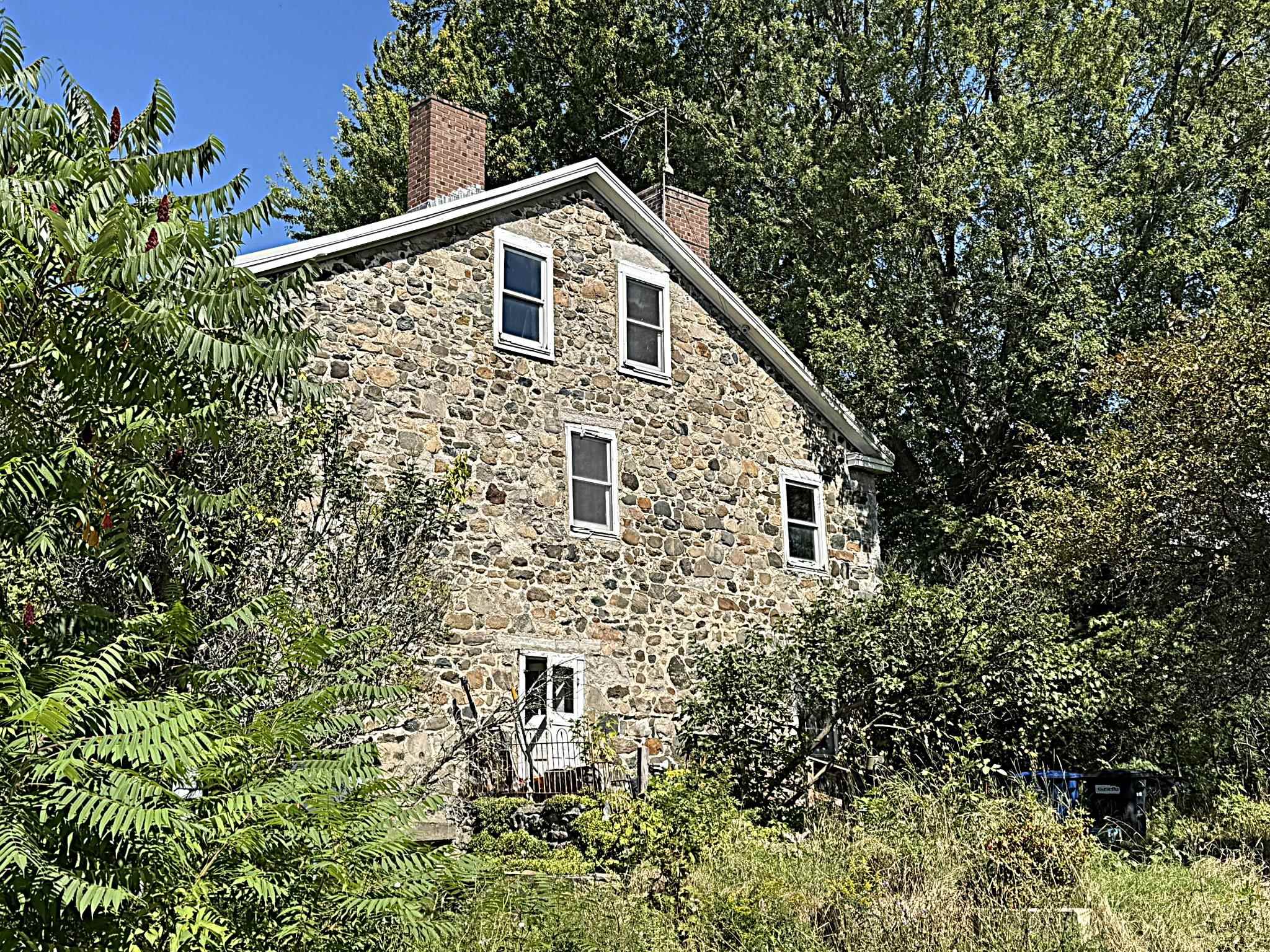 Stone house with a steep gabled roof and brick chimneys, surrounded by dense trees.