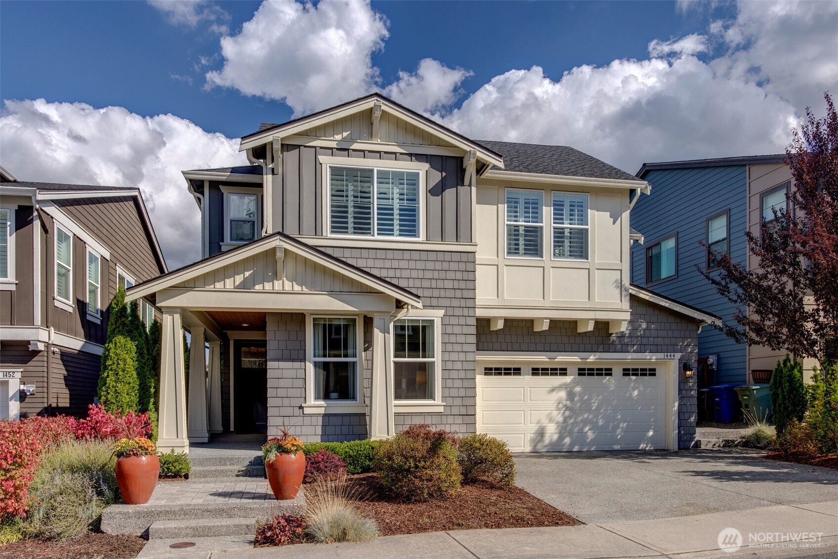 Two-story gray-shingled home with a covered entry, double garage, and landscaped front yard.